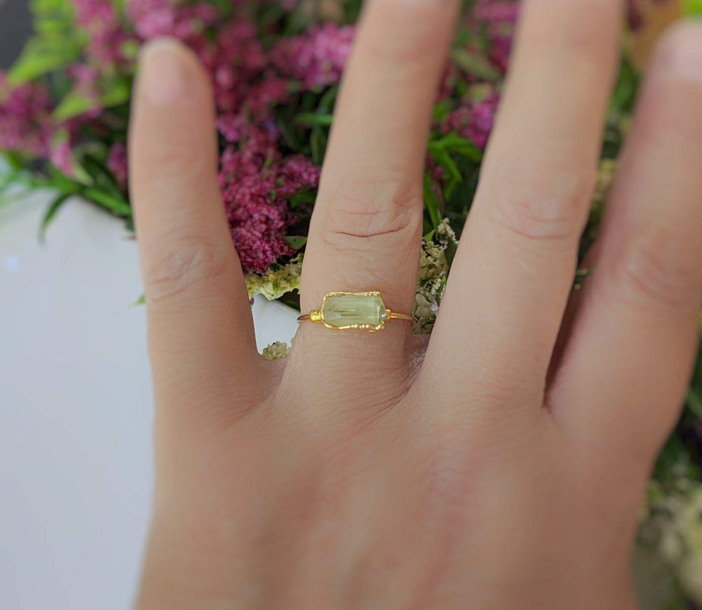 Raw yellow Apatite ring on a hand, featuring a 14k gold filled band and set against a backdrop of flowers.