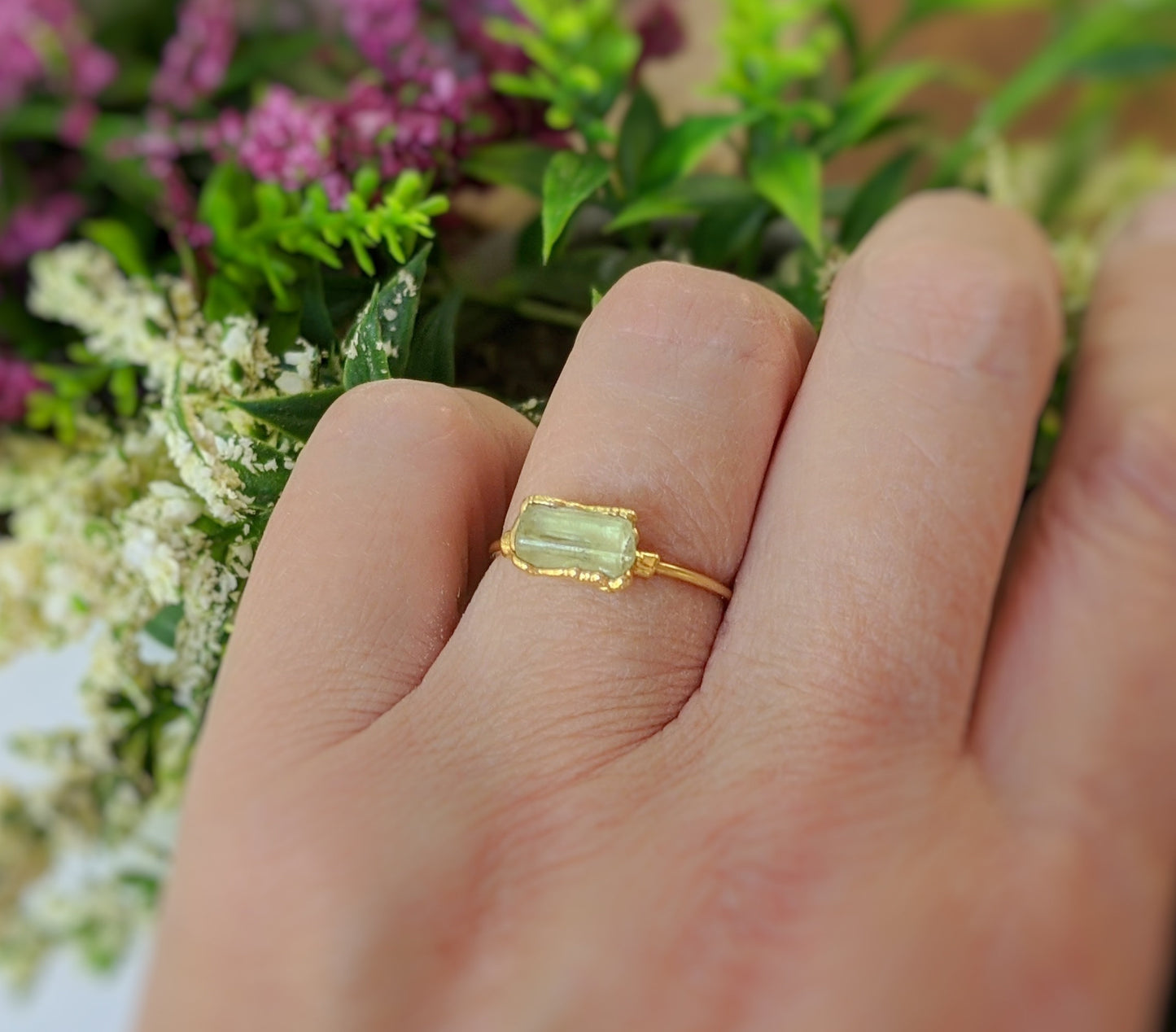 Raw yellow Apatite ring on a hand, featuring a 14k gold filled band and surrounded by flowers.