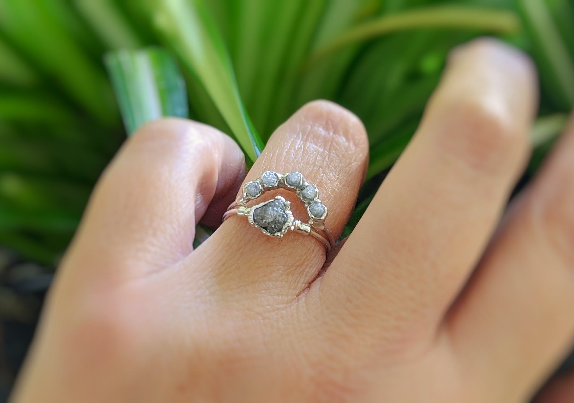 Raw diamond Chevron wedding ring set displayed on a hand, featuring silver-grey diamonds and a natural design.