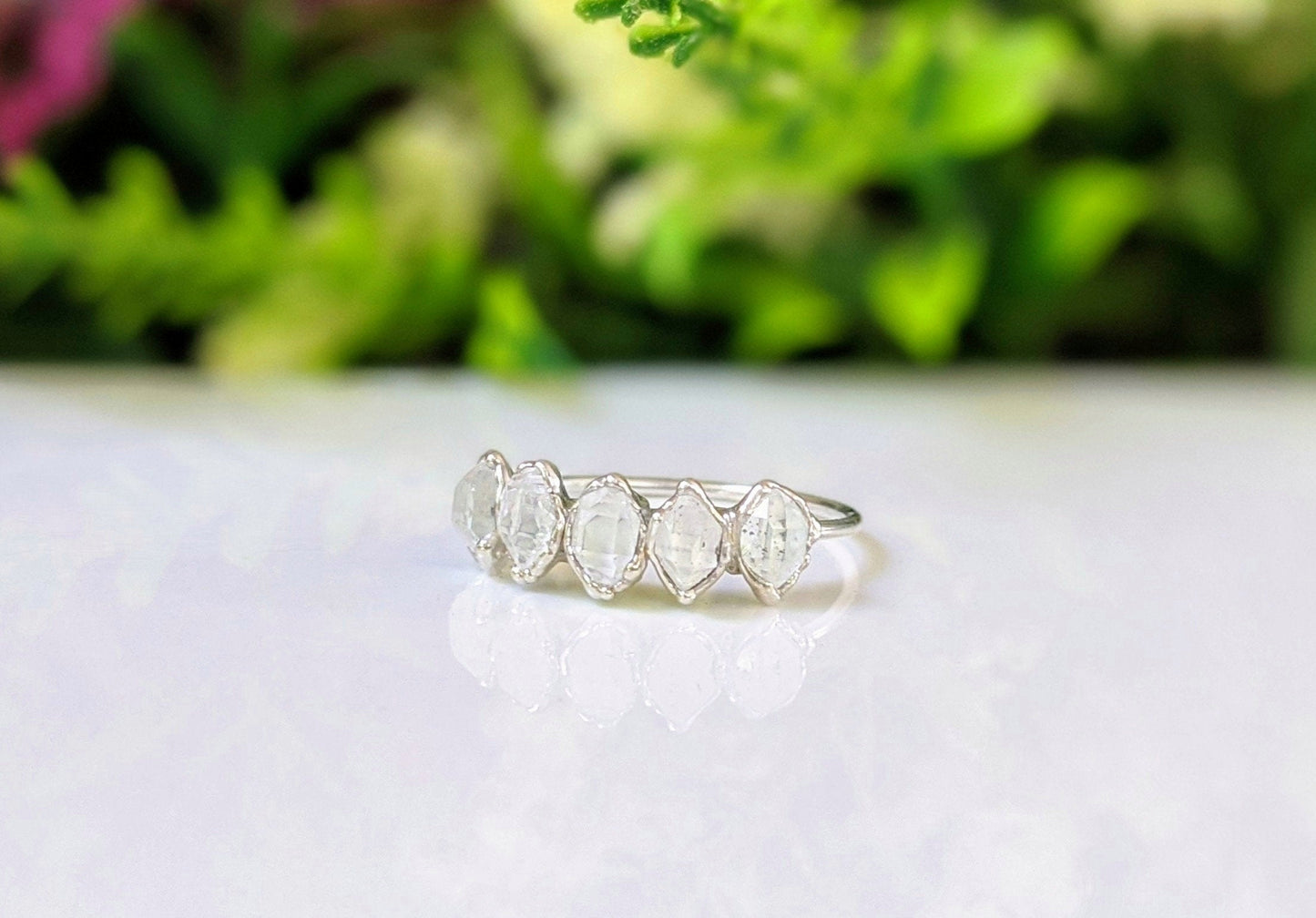 Handcrafted silver eternity ring featuring five raw Herkimer diamonds on a sterling silver band, set against greenery.