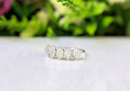 Handcrafted silver eternity ring featuring five raw Herkimer diamonds on a sterling silver band, set against greenery.