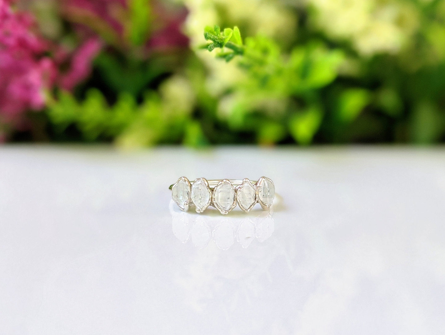 Herkimer diamond silver eternity ring featuring five raw diamonds on a delicate silver band, surrounded by colorful floral backdrop.