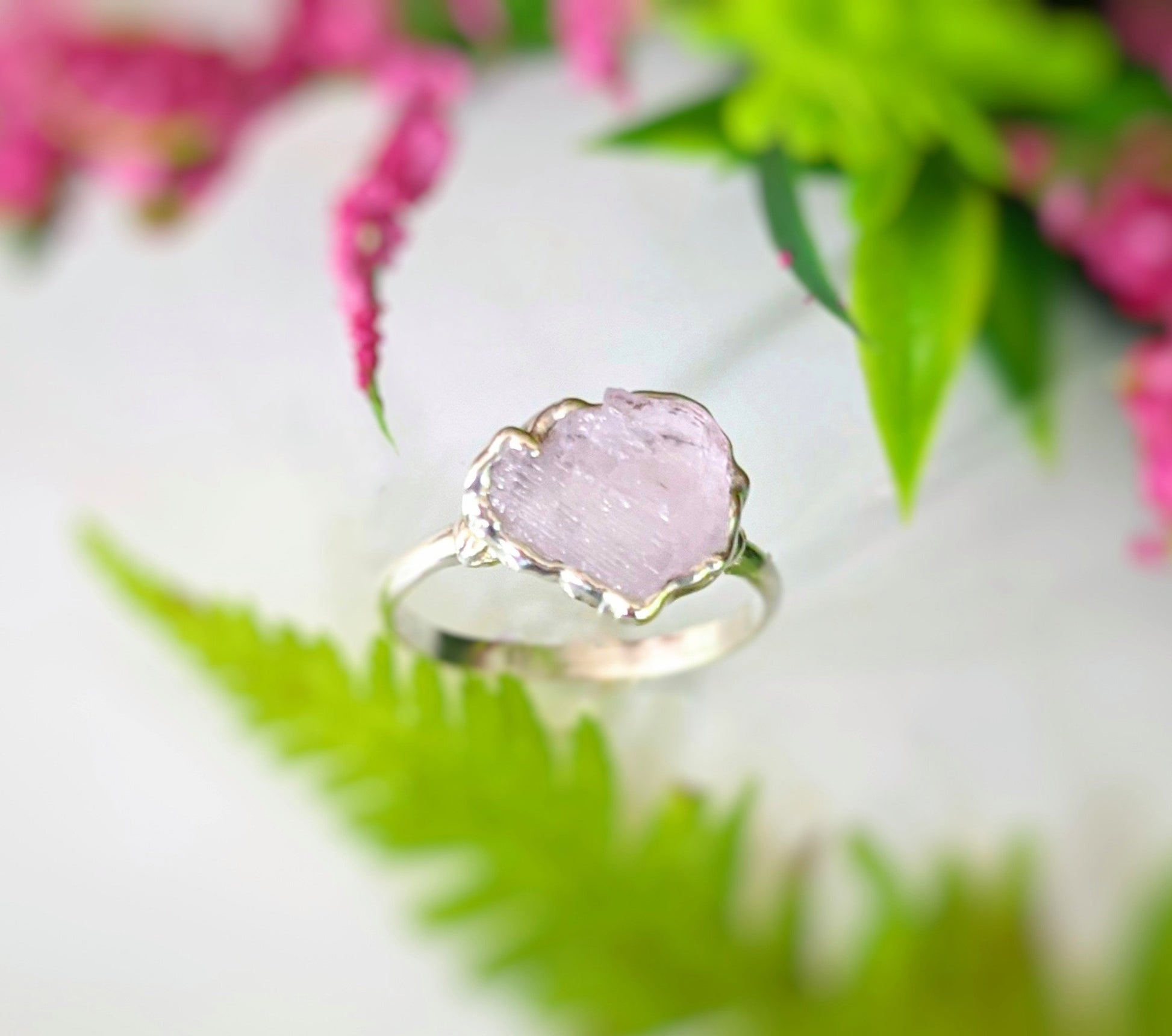Handcrafted raw pink Morganite ring set on a silver band, surrounded by greenery and floral accents.