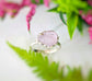 Handcrafted raw pink Morganite ring set on a silver band, surrounded by greenery and floral accents.