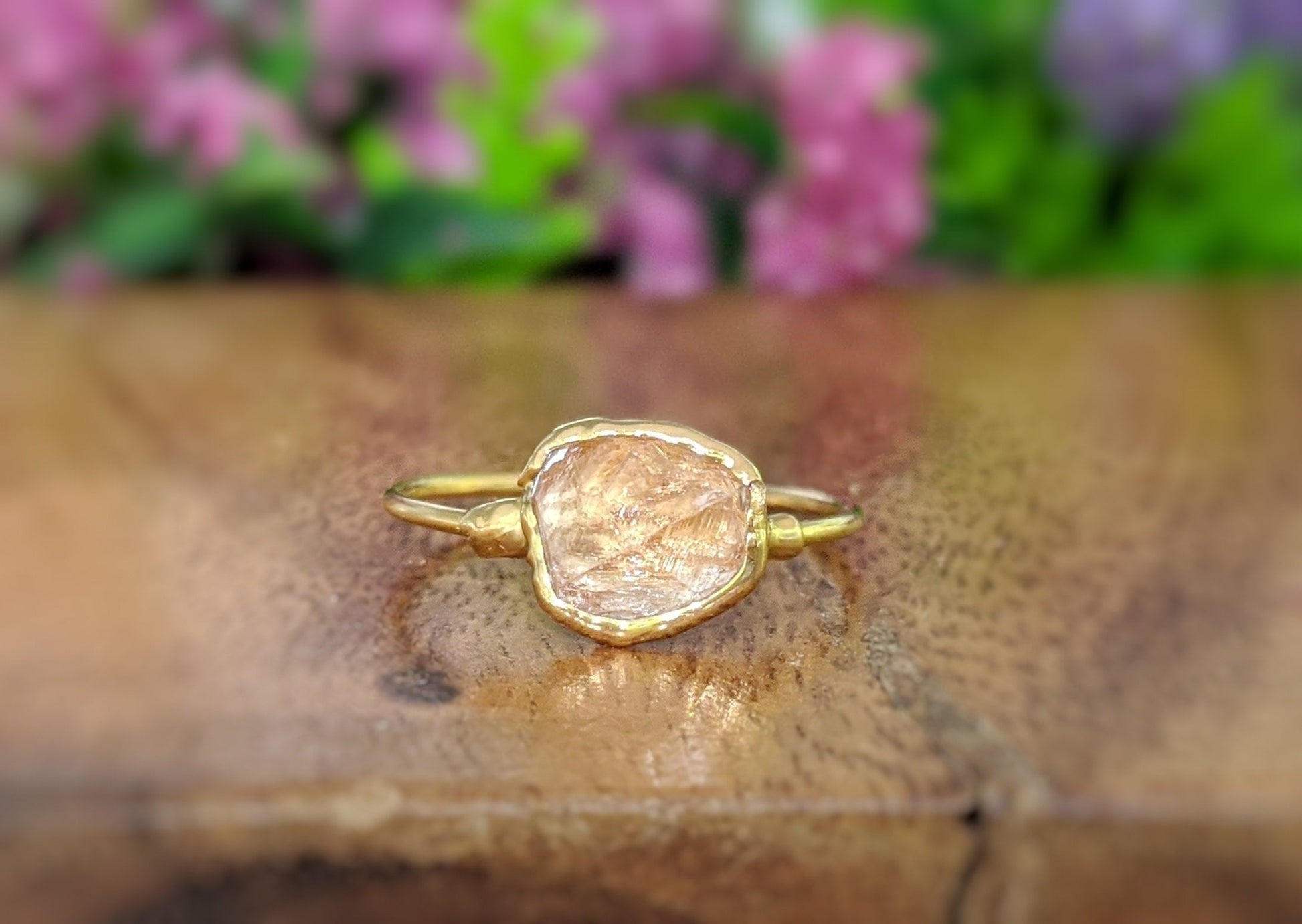 Raw Hessonite Garnet ring on a wooden surface, featuring a gold band and blurred floral background.