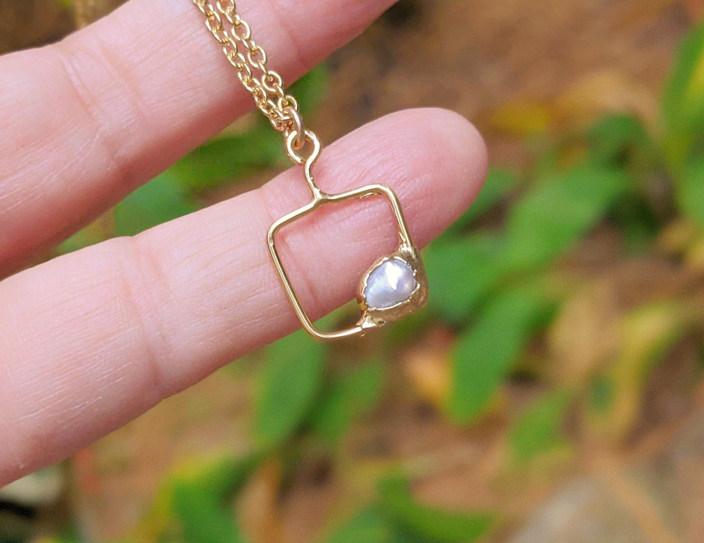 Personalized family birthstone necklace with square pendant and raw gemstone, held in a hand outdoors.