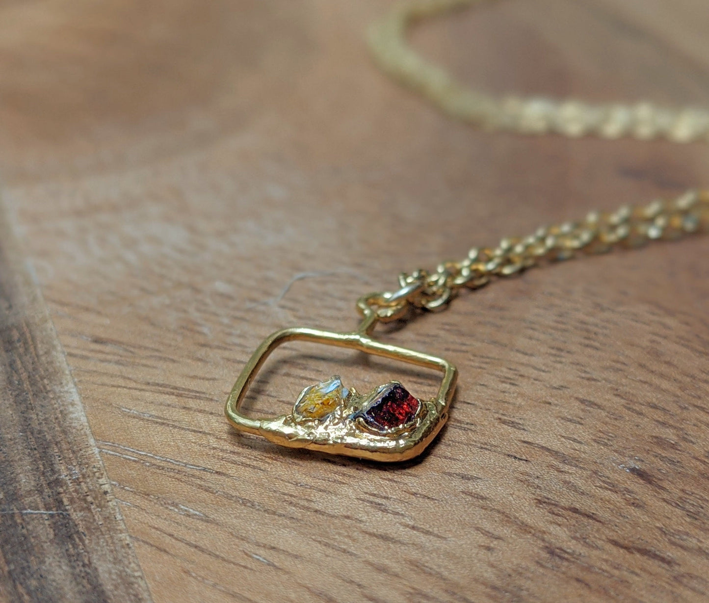 Close-up of a personalized gold necklace featuring raw gemstones in a framed pendant on a wooden surface.