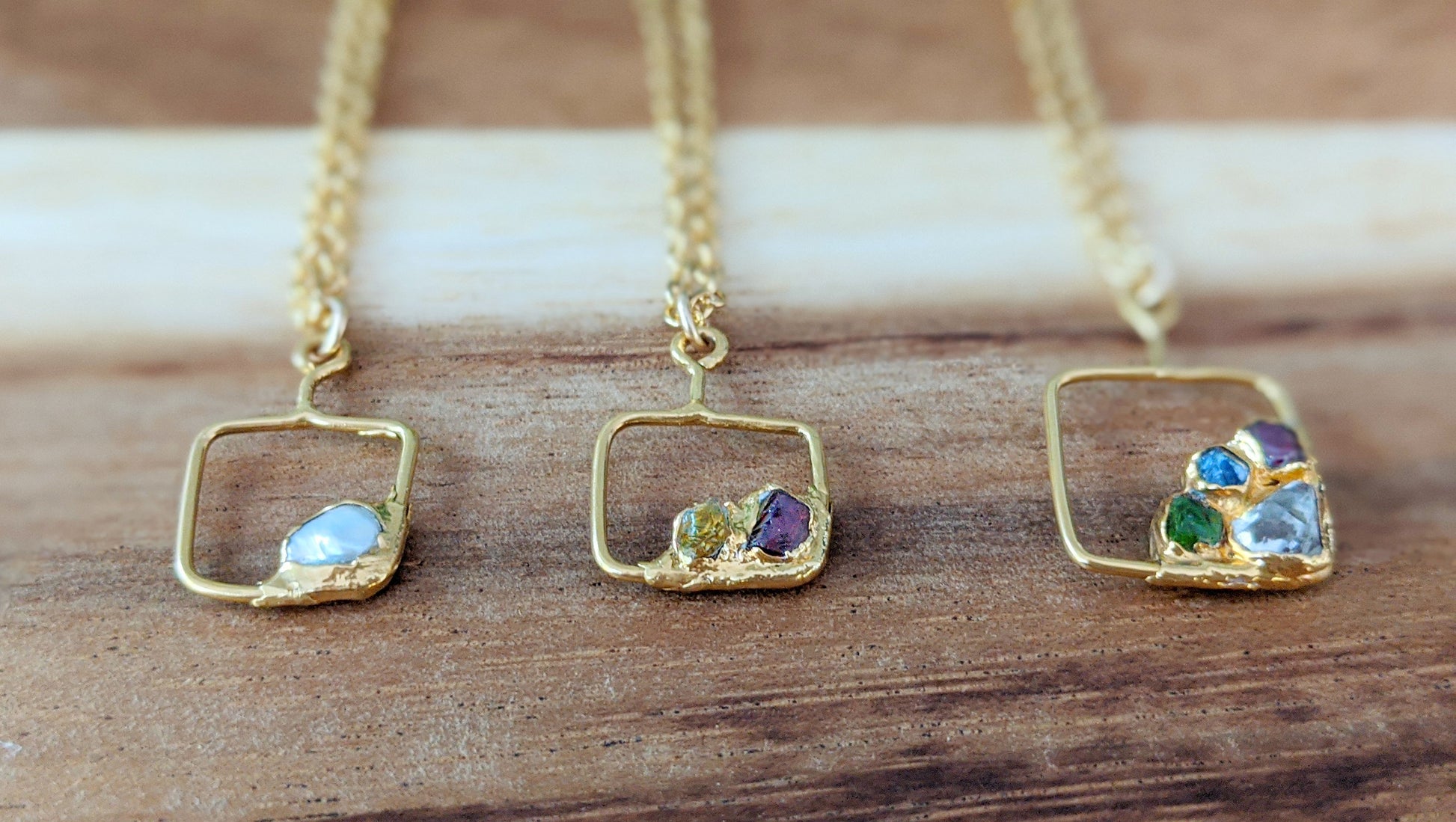 Three unique gold-filled family birthstone necklaces featuring raw gemstones in square pendants.
