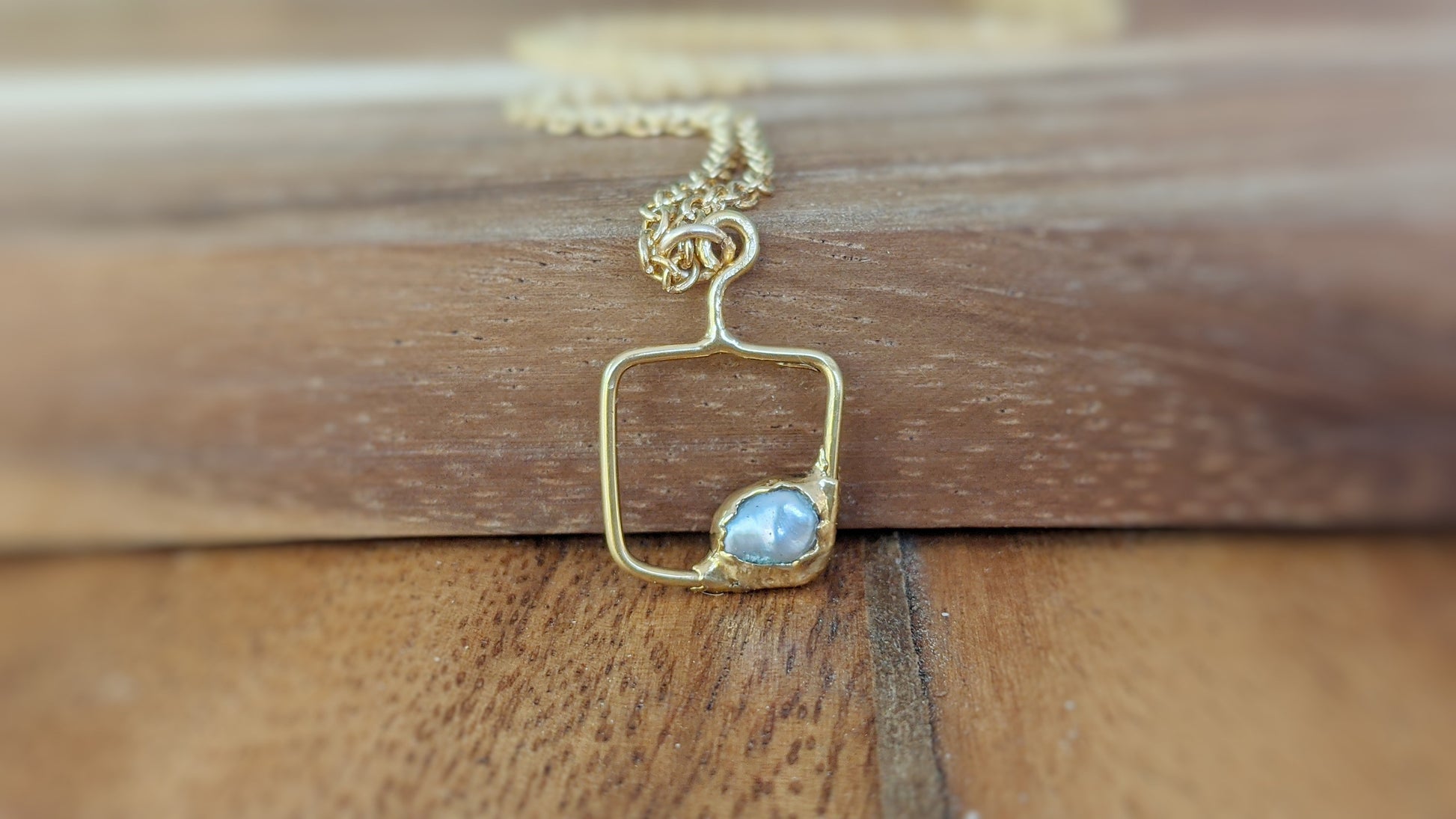 14k gold filled square pendant necklace with raw gemstone on wood background.