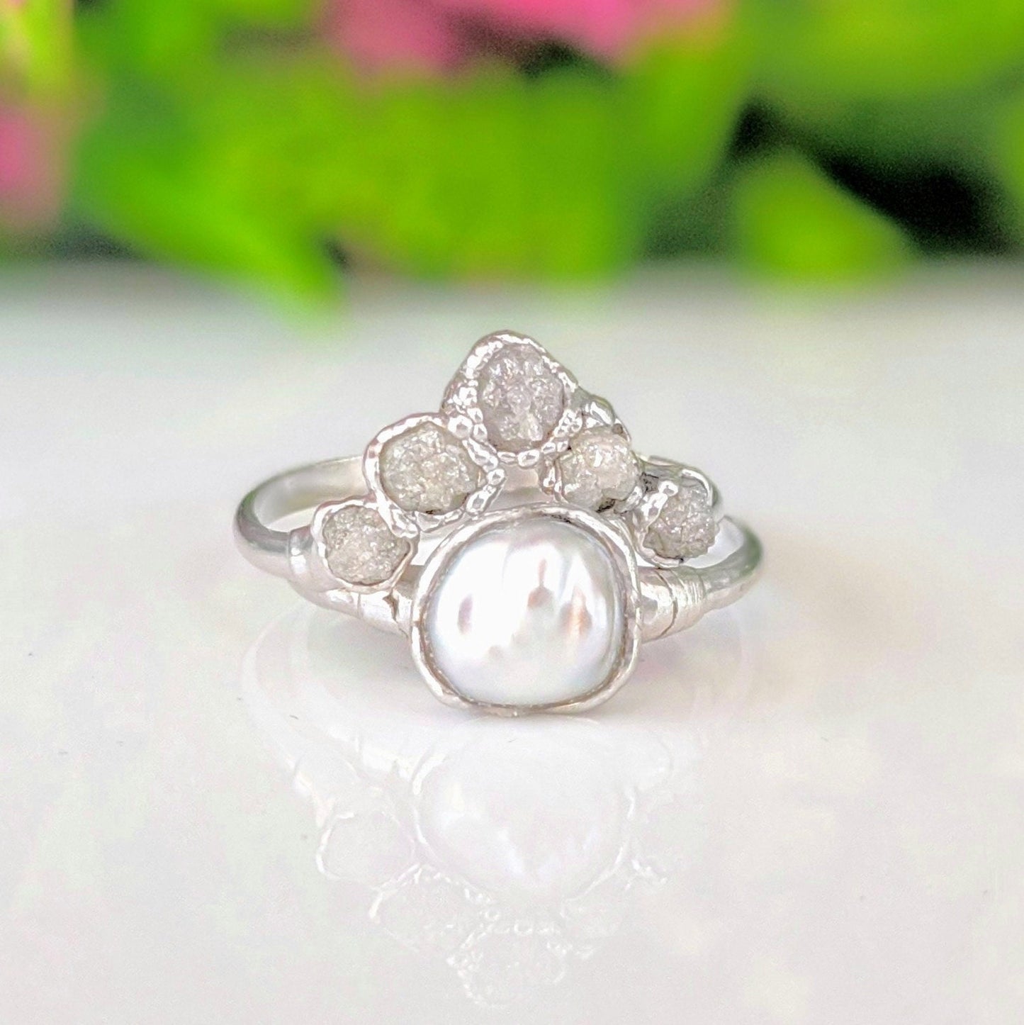 Raw diamond and Keshi pearl Chevron wedding ring set on a reflective surface, showcasing its unique handcrafted design.