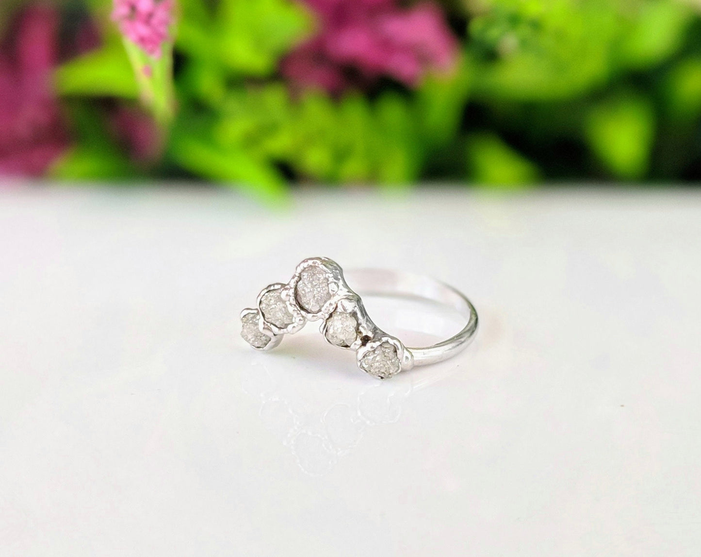 Handcrafted raw diamond Chevron wedding ring set on a polished surface with green foliage in the background.