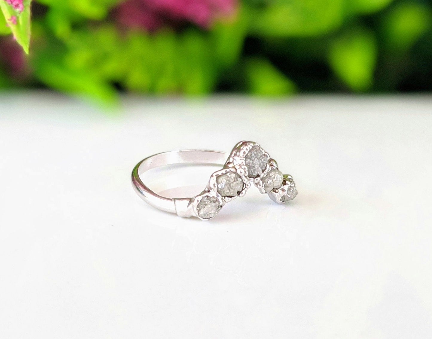 Chevron wedding ring featuring raw diamonds set in sterling silver, against a blurred floral background.