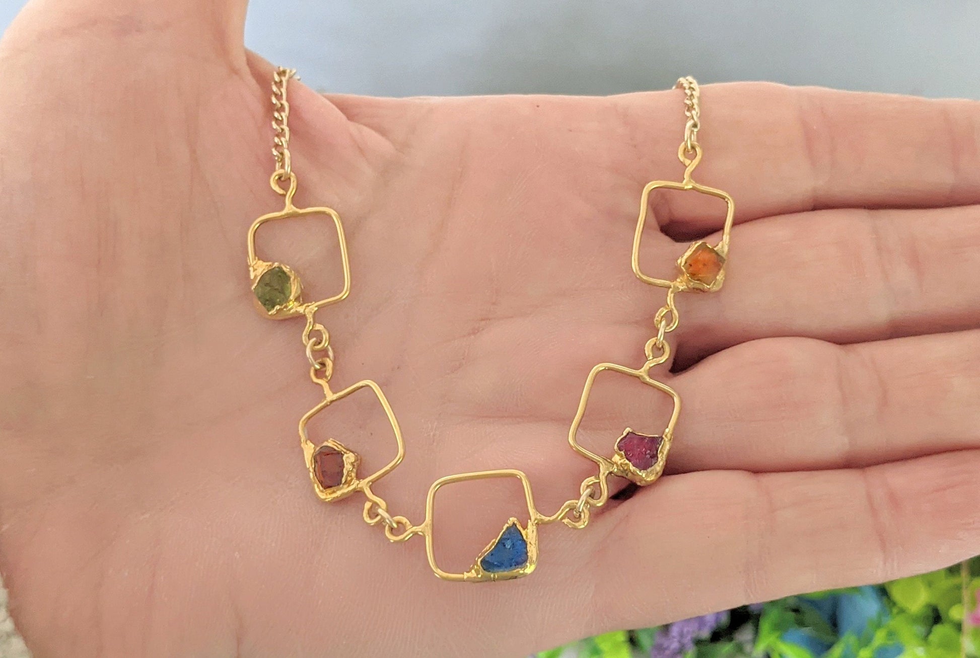 Personalized family birthstone necklace with raw gemstones displayed on a hand, featuring gold square charms.