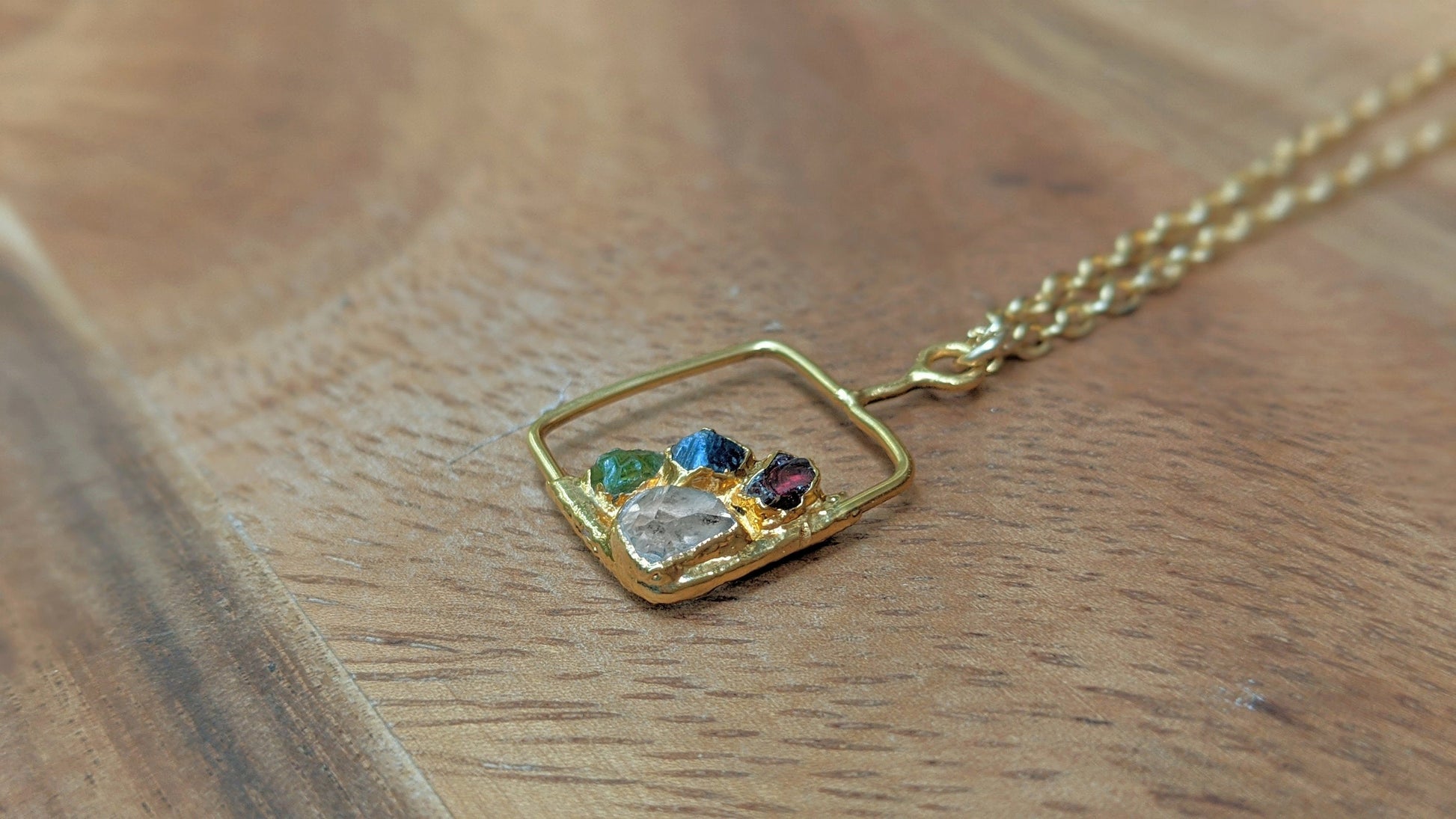 Personalized family birthstone necklace with raw gemstones and a gold square pendant on a chain.