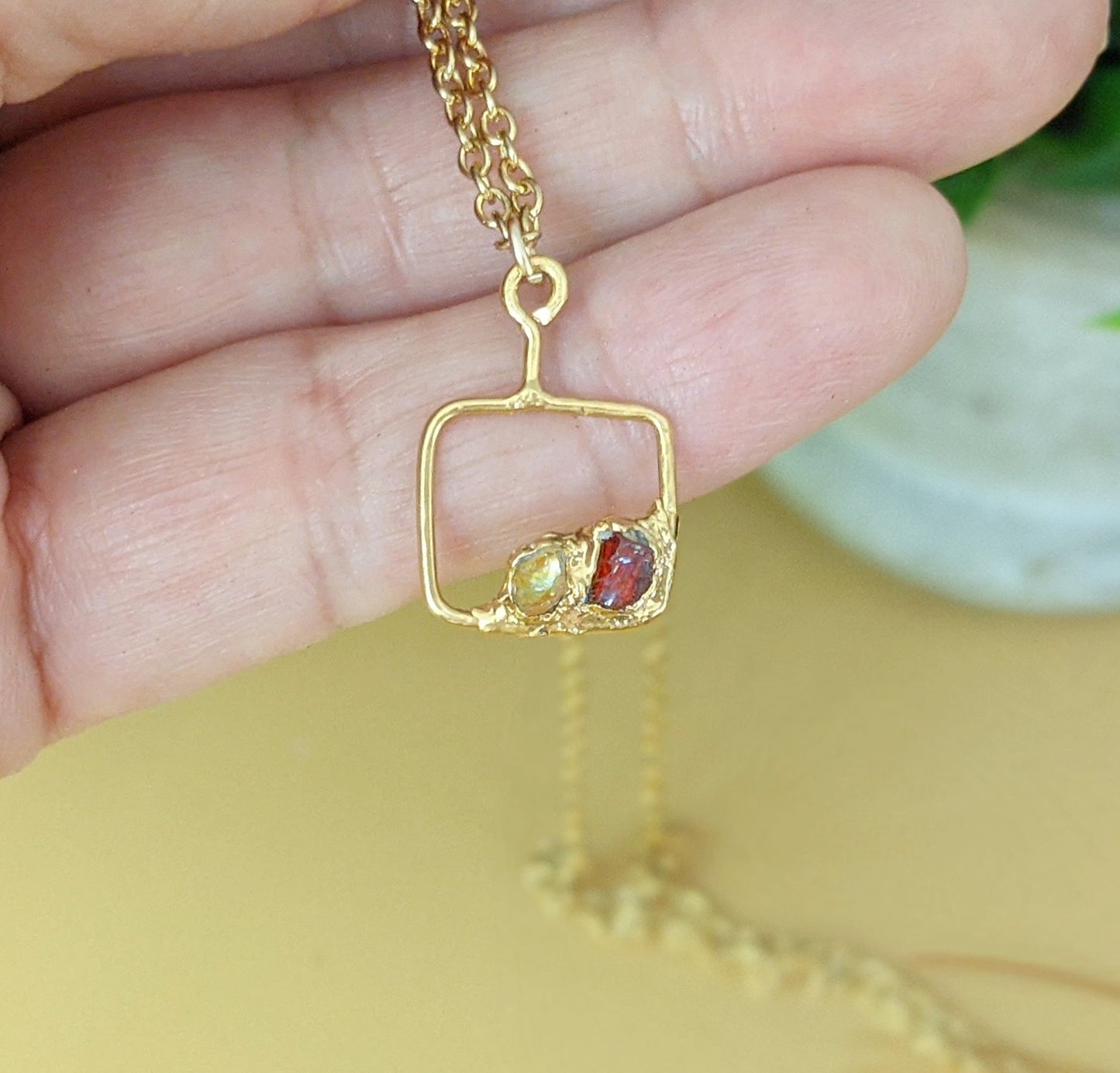 Hand holding a custom Family Birthstone necklace with a gold-filled pendant and colorful raw gemstones.