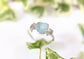 Raw Aquamarine and diamond twig ring on sterling silver band with greenery in background.