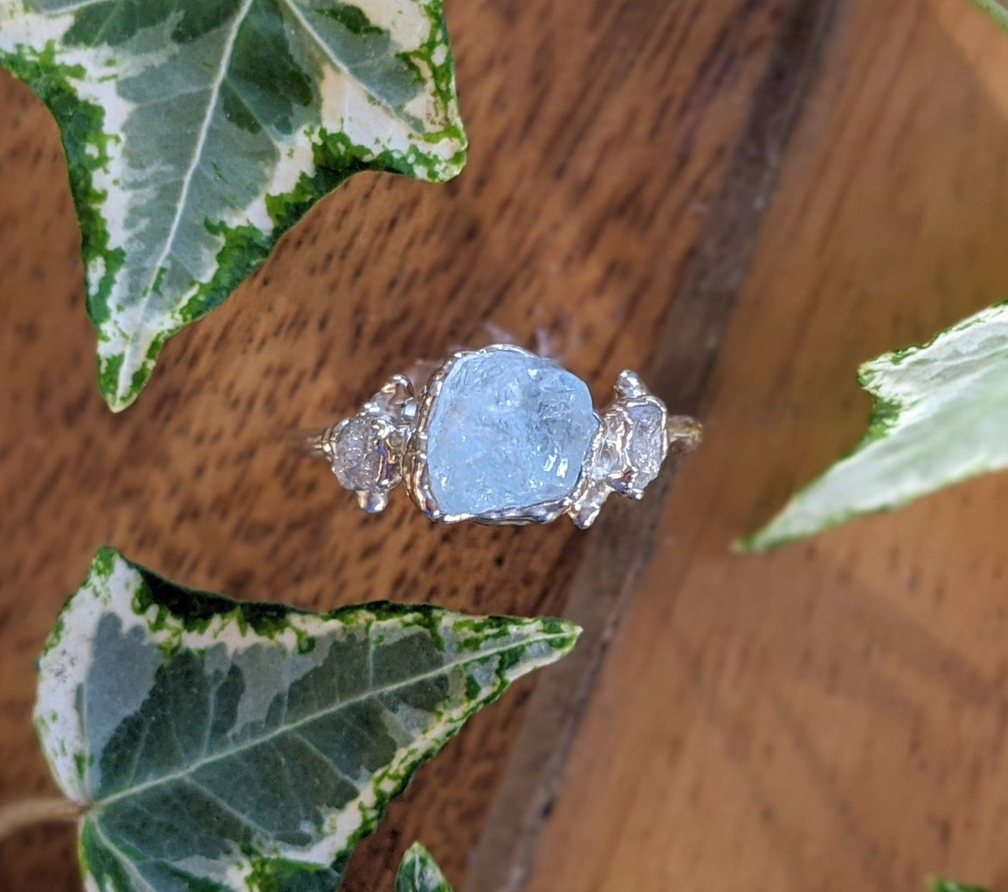 Raw aquamarine and diamond twig ring on wooden surface surrounded by ivy leaves, perfect unique engagement ring.