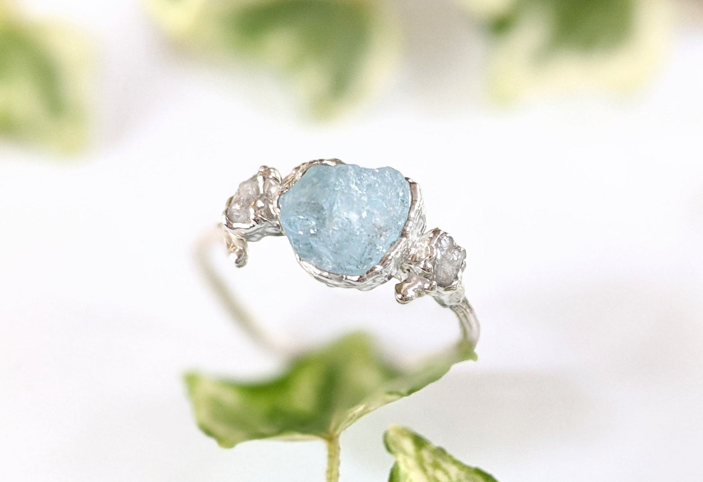 Raw Aquamarine and diamond twig ring on a leafy background, showcasing a unique nature-inspired design.