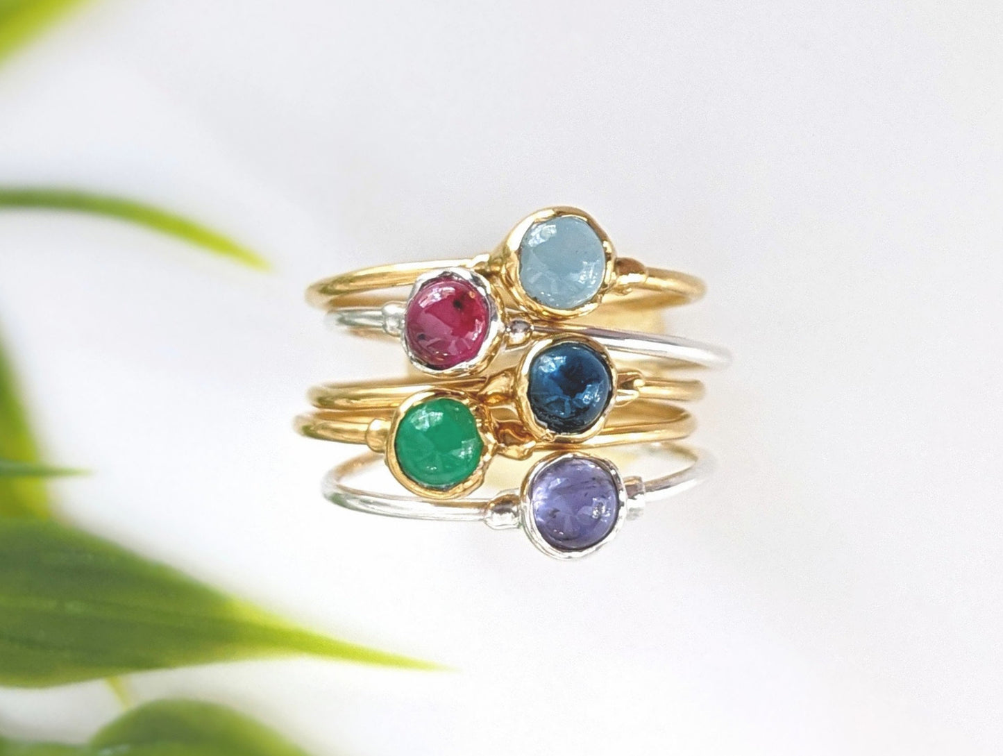 Colorful multi-gemstone stacking rings featuring red, green, blue, and purple stones on gold and silver bands.