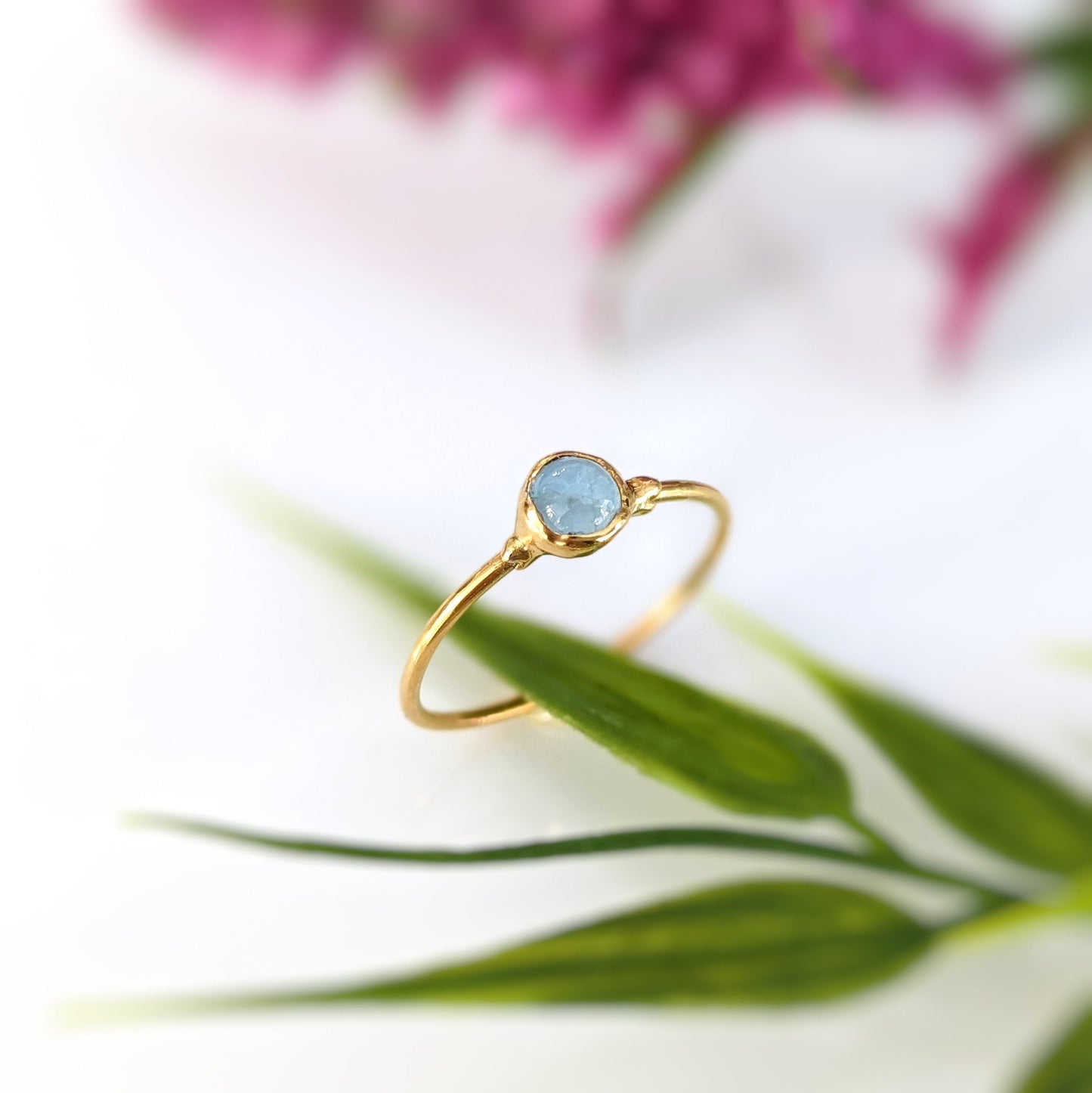Dainty Aquamarine stacking ring on a gold band, featuring a natural 4mm stone, surrounded by delicate greenery.