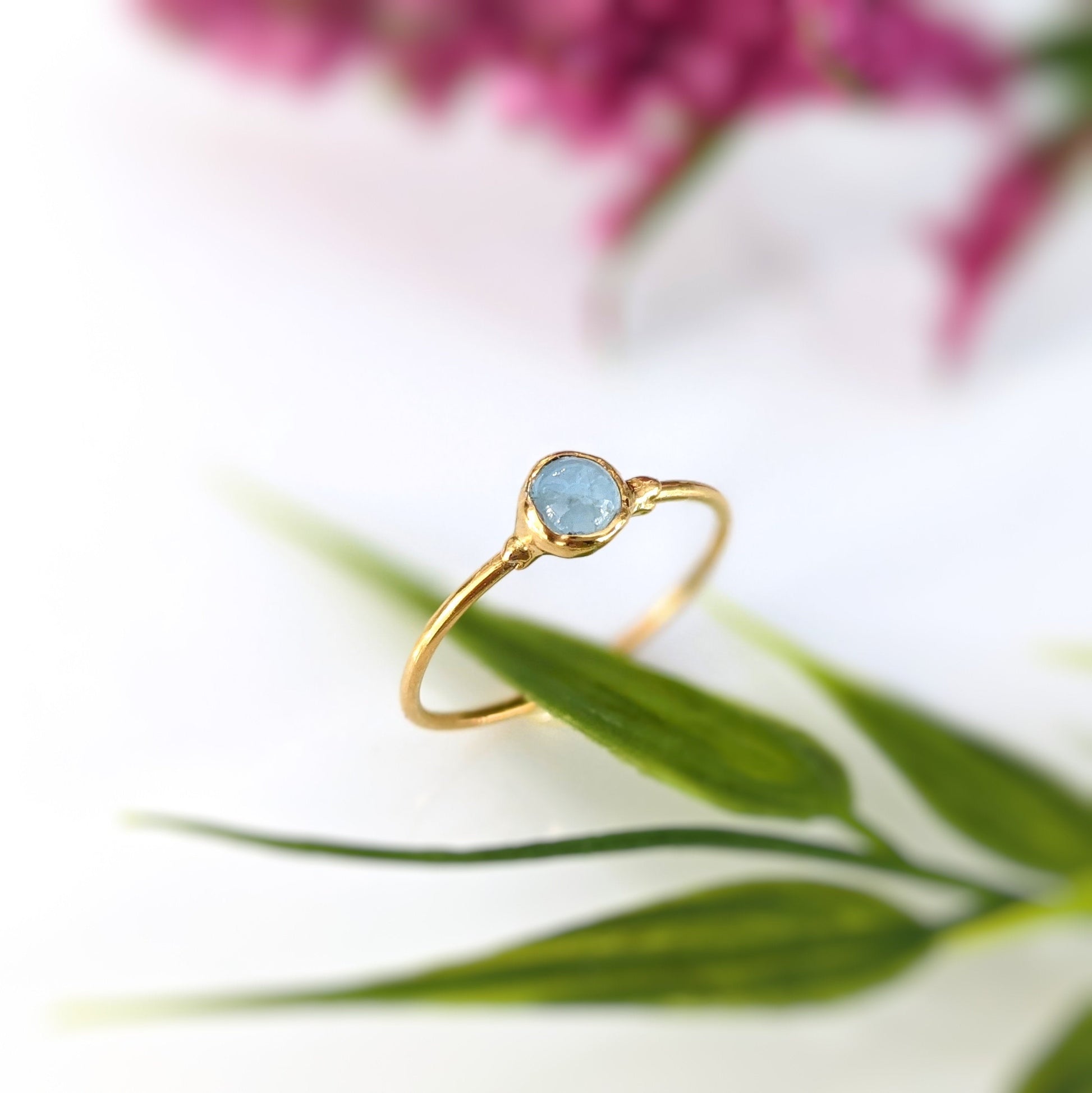 Dainty Aquamarine stacking ring on a gold band, featuring a natural 4mm stone, surrounded by delicate greenery.