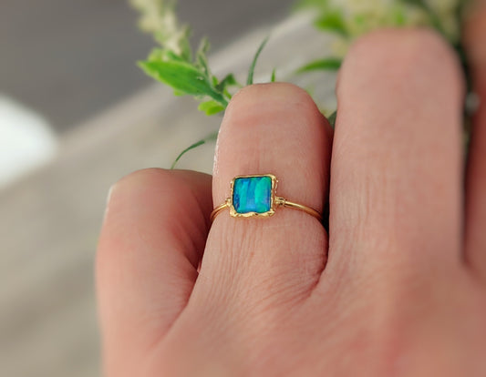 Close-up of a hand wearing a blue Opal ring in 18k gold, showcasing the Aqua blue stone and delicate band.