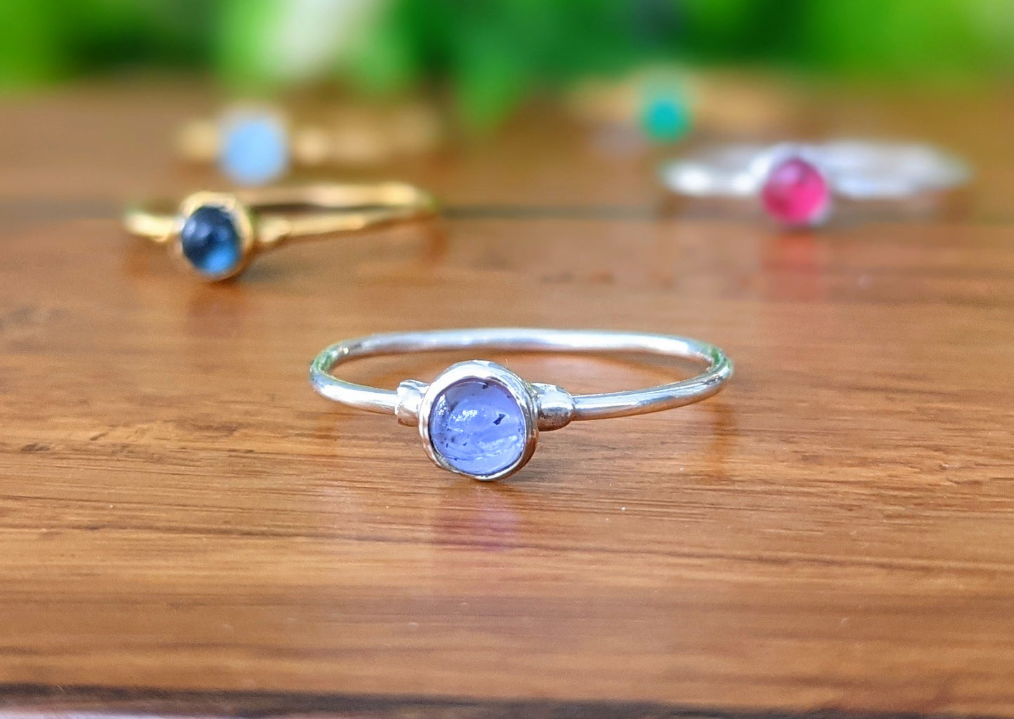 Dainty Tanzanite stacking ring on wooden surface, showcasing a natural purple/blue gemstone in a minimalistic design.