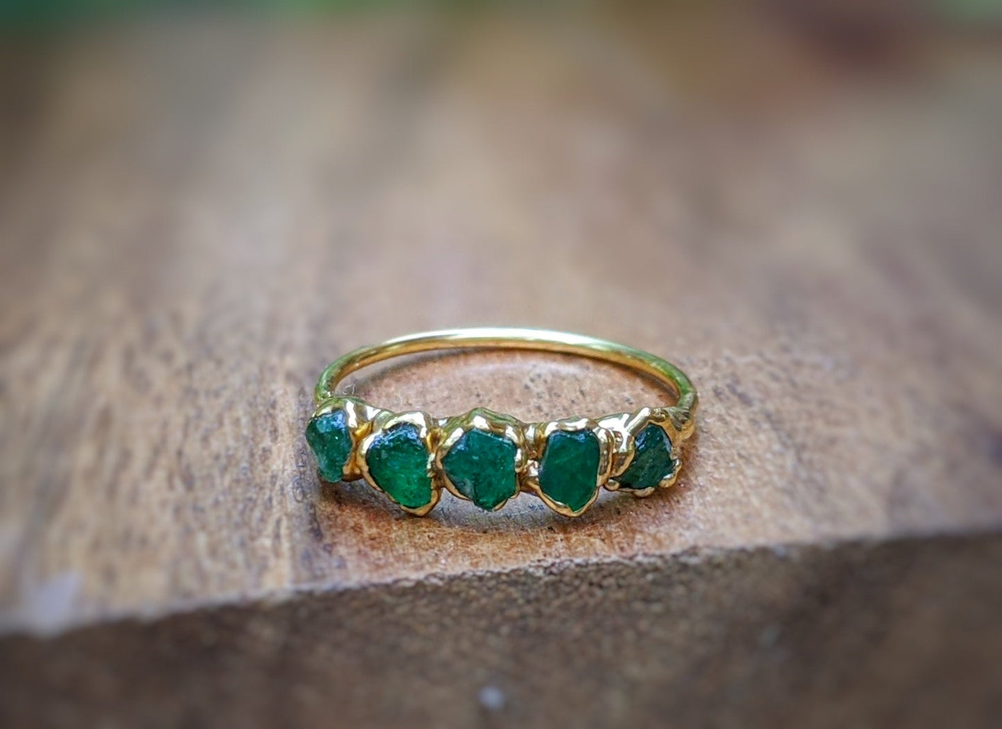 Raw Emerald Multi-stone Ring on a wooden background, showcasing 5-7 green Emeralds set in 14k Gold band.
