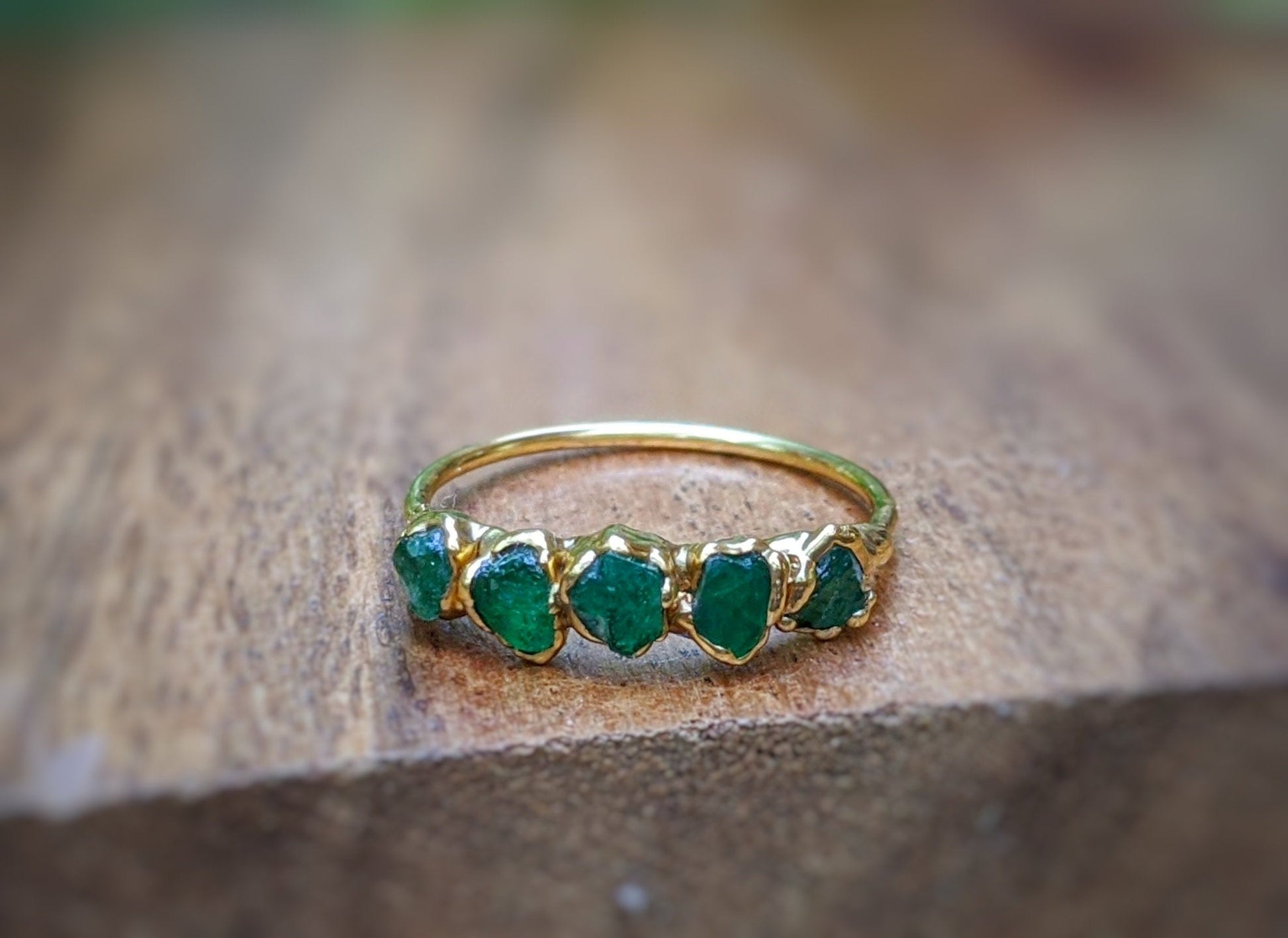 Raw Emerald Multi-stone Ring on a wooden background, showcasing 5-7 green Emeralds set in 14k Gold band.