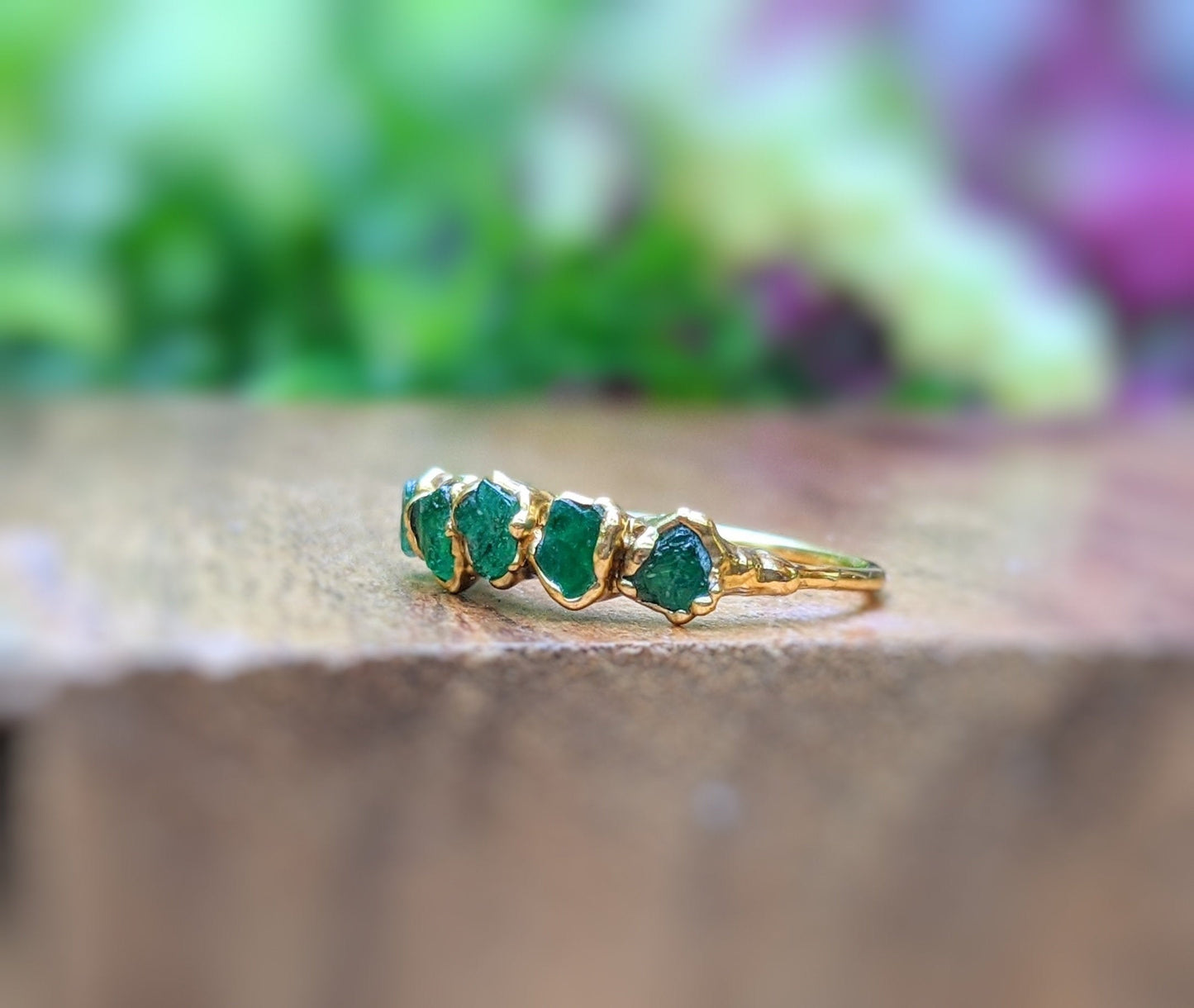 Raw Emerald multi-stone ring on a wooden surface, featuring 4 green emeralds on a 14k gold band.