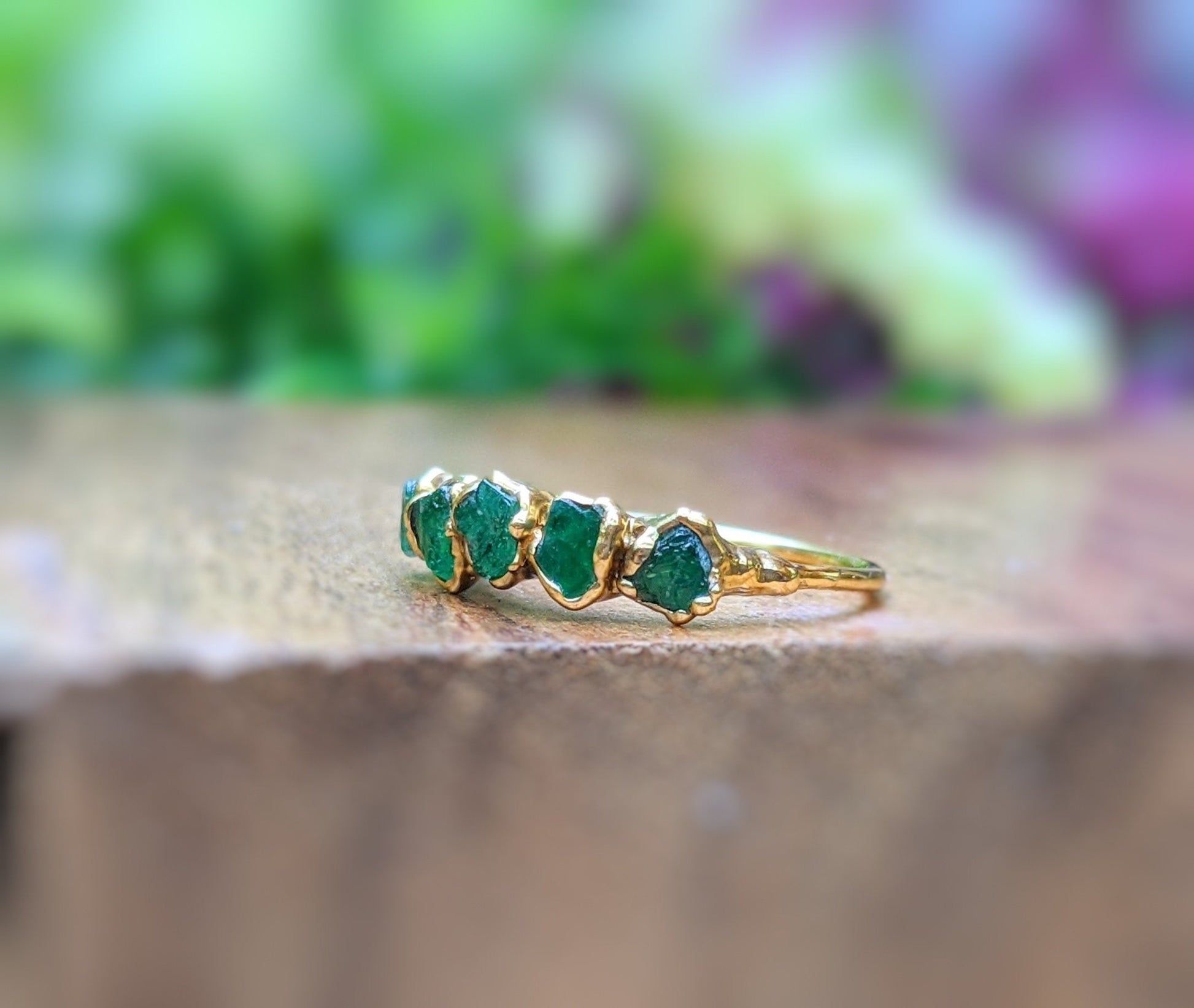 Raw Emerald multi-stone ring on a wooden surface, featuring 4 green emeralds on a 14k gold band.