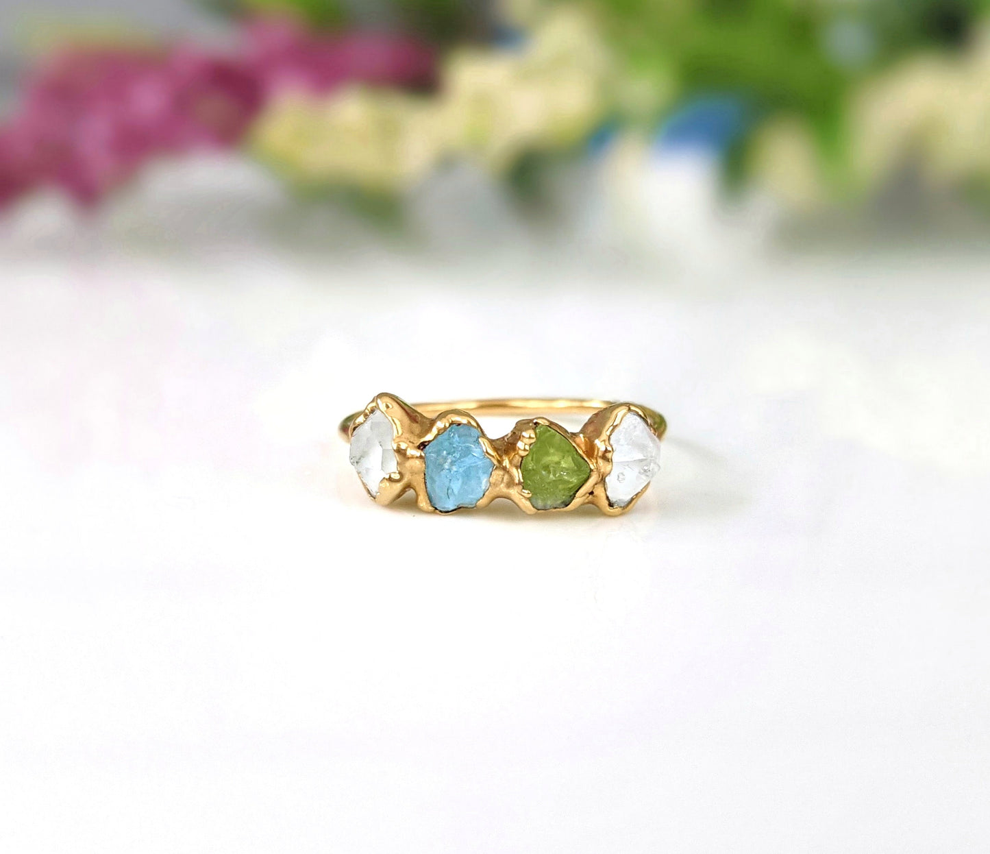 Raw gemstone Mother's ring with blue, green, and clear stones set in a gold band, symbolizing family birthstones.