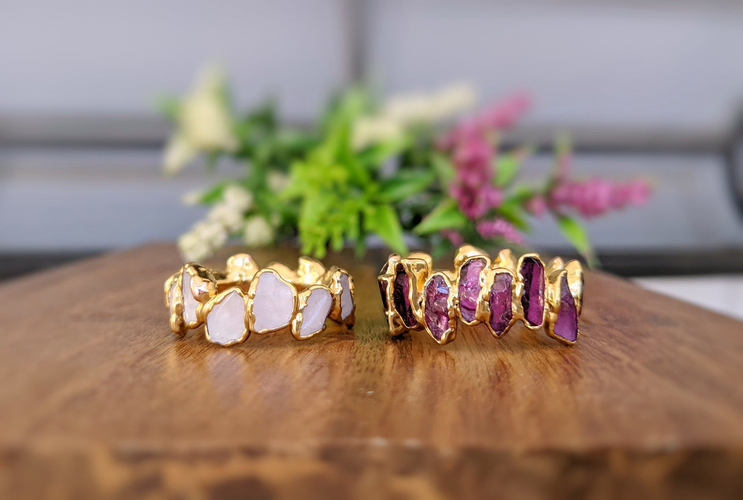 Two gold-filled eternity rings featuring rose quartz and amethyst stones on a wooden surface.