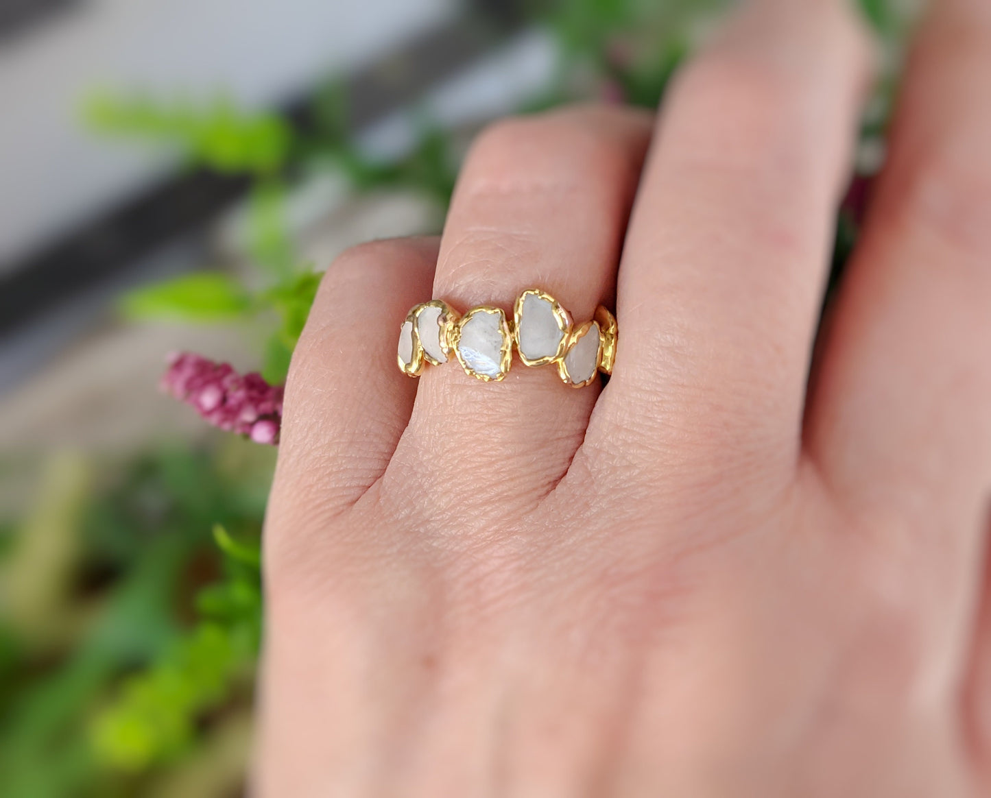 Rose Quartz eternity gold ring showcasing unique gemstone design on a hand with green foliage background.