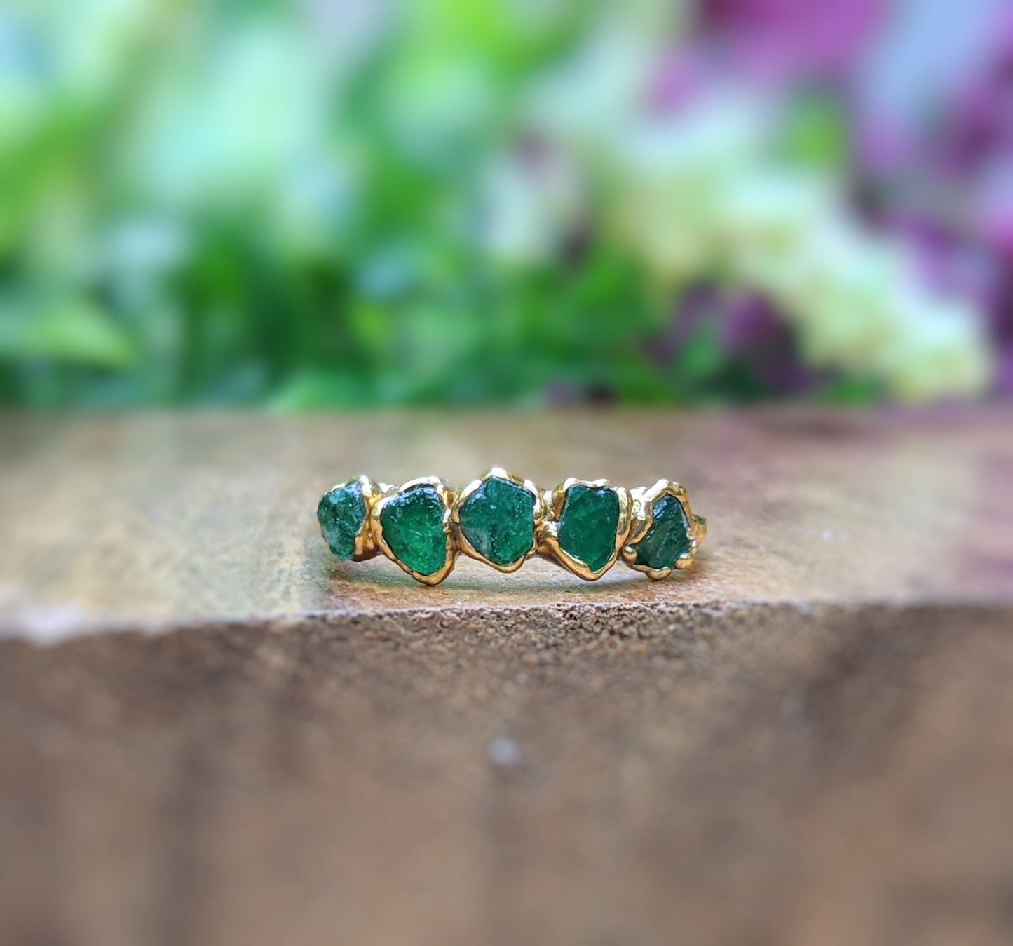 Raw emerald multi-stone ring on a wooden surface, featuring 5-7 handcrafted emeralds on a 14k gold filled band.