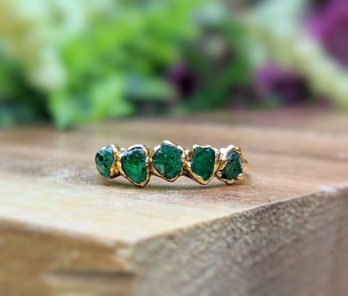 Handcrafted raw emerald multi-stone ring on a wooden surface, featuring 5-7 small emeralds set in 14k gold.