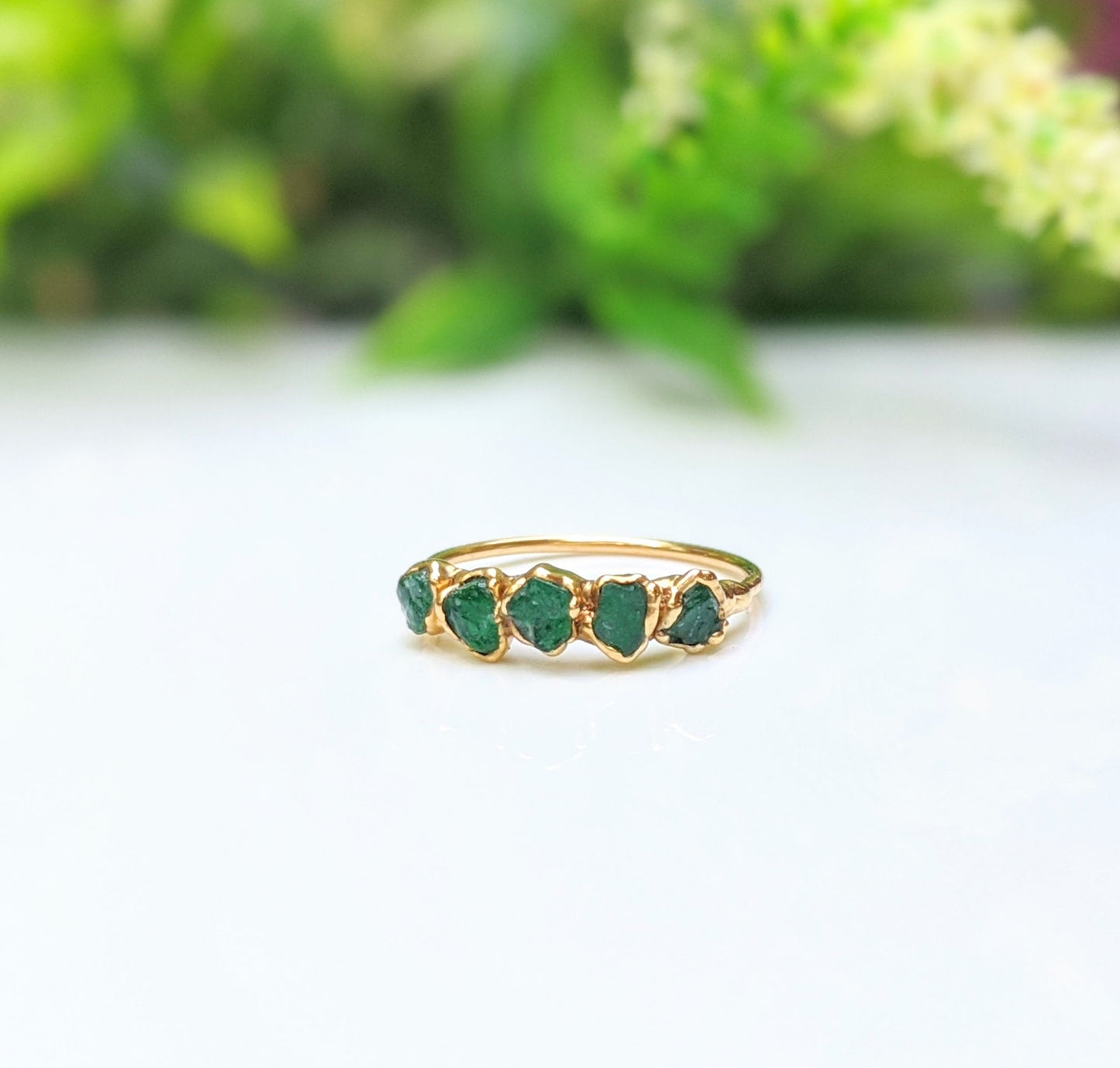 Raw emerald multi-stone ring on a gold band, featuring 5-7 unique green emeralds, perfect for May birthdays.