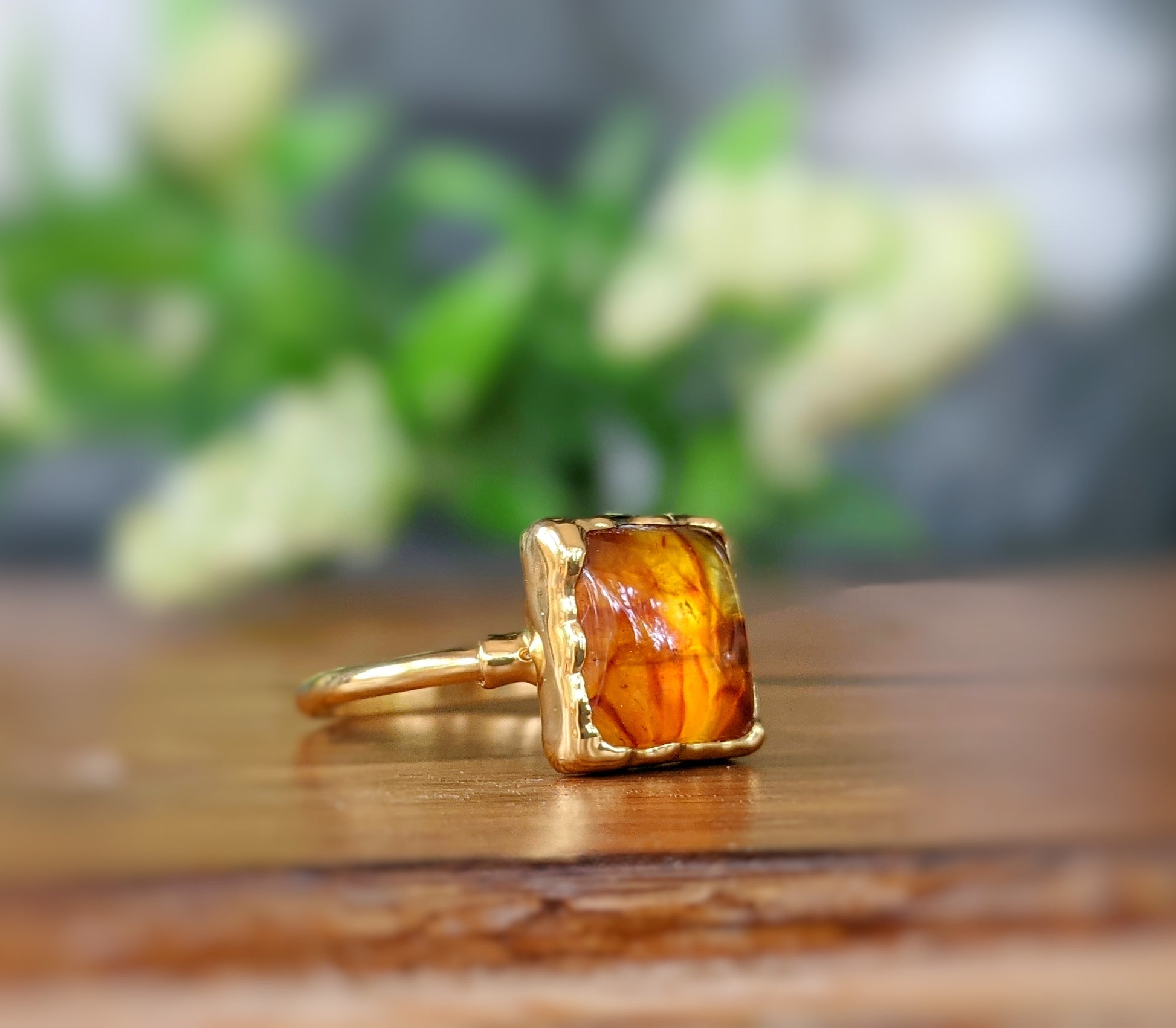 Square Baltic Amber gold ring on wooden surface, featuring a honey-colored stone set on a gold-filled band.