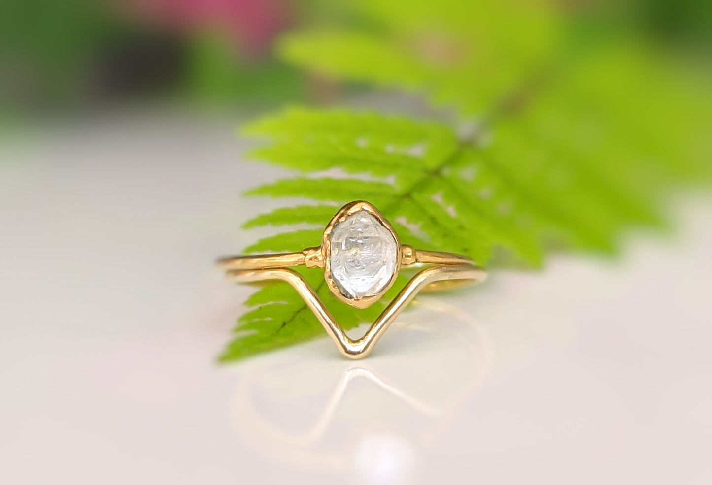Gold Herkimer Diamond Chevron engagement ring set atop green fern leaves, symbolizing love and uniqueness.