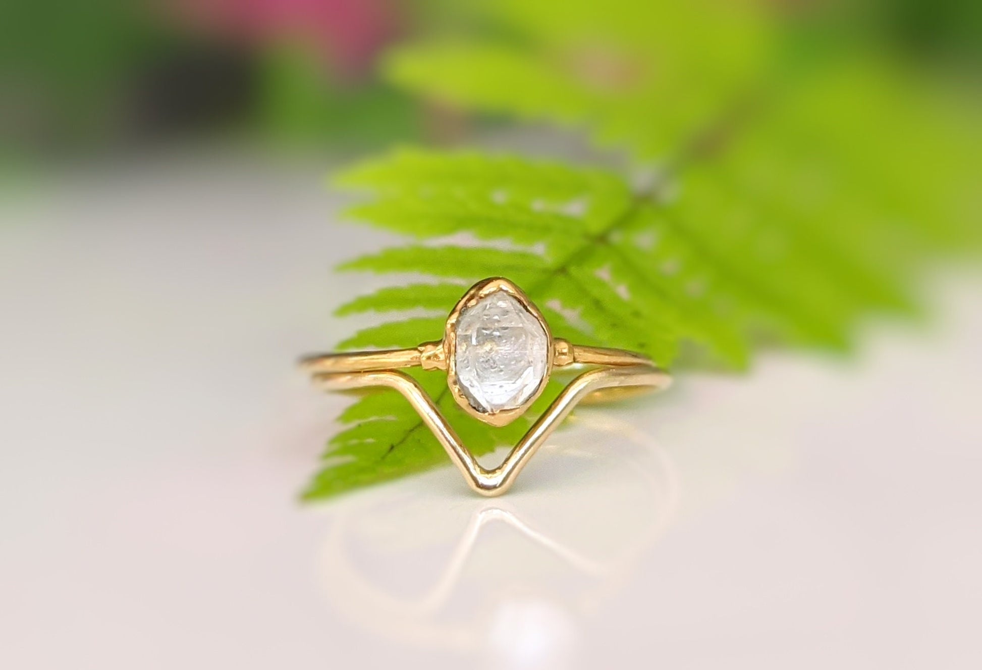 Gold Herkimer Diamond Chevron engagement ring set atop green fern leaves, symbolizing love and uniqueness.