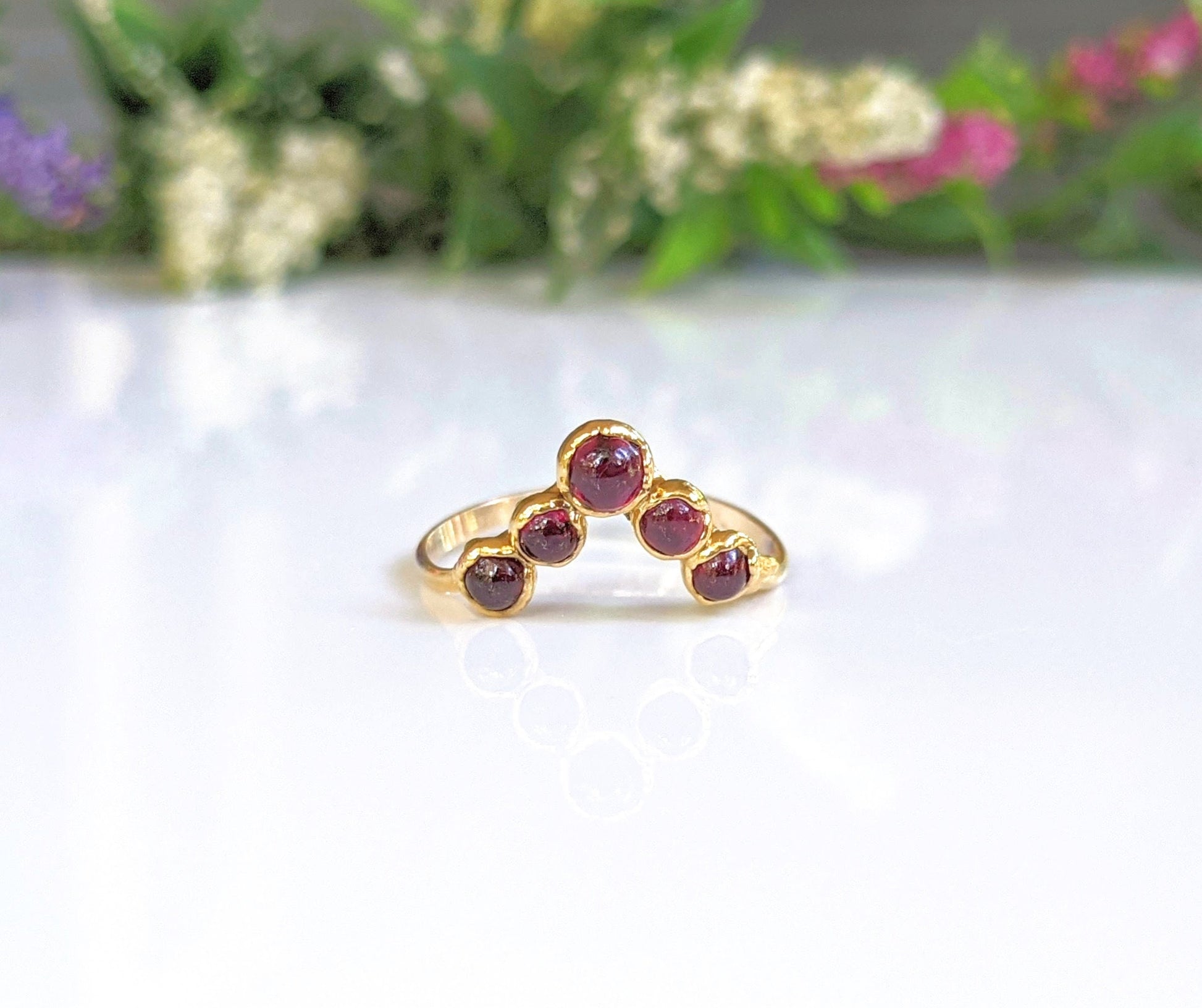Handcrafted gold ring featuring natural Ruby stones on a reflective surface with floral background.