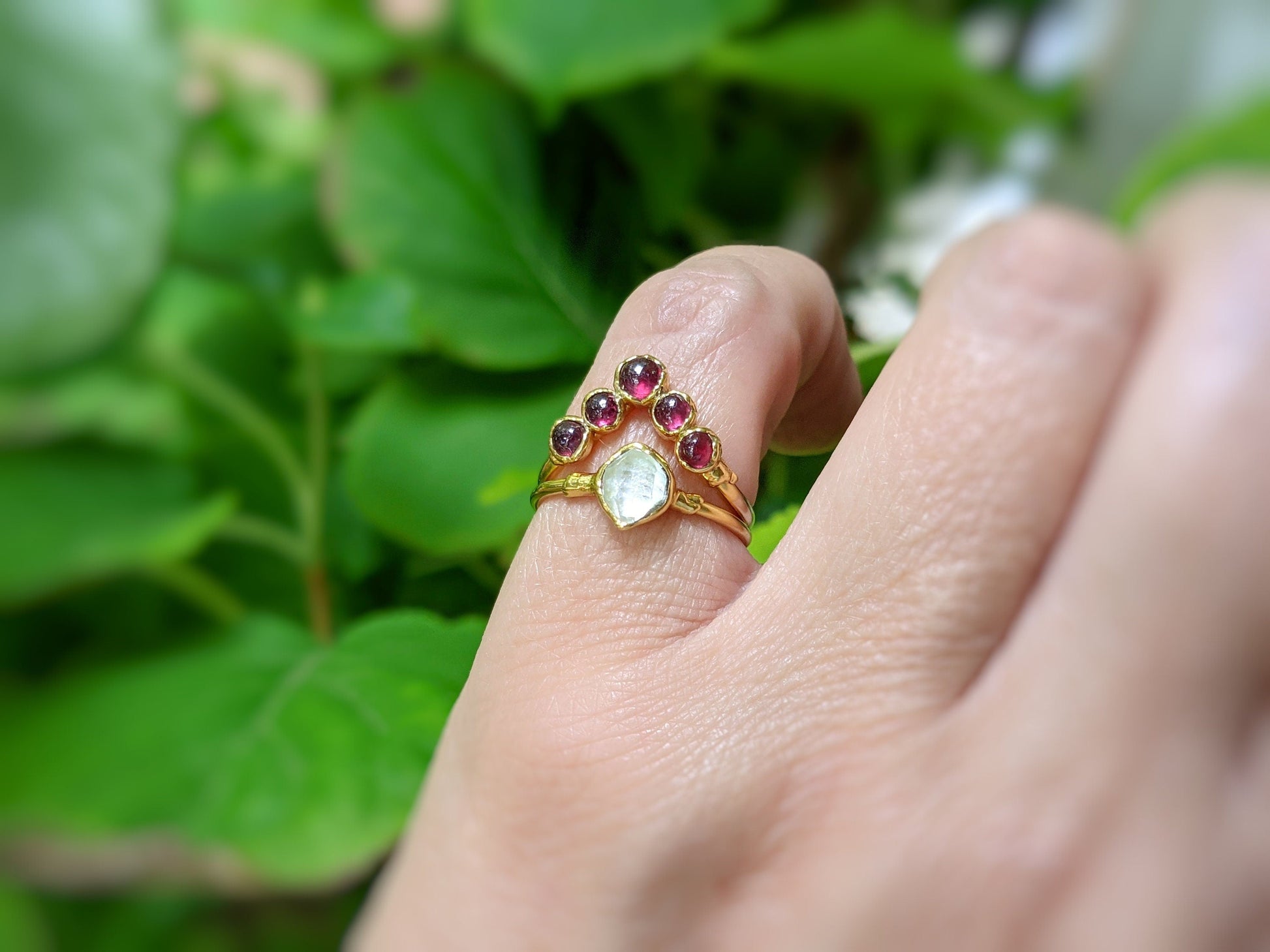 Natural ruby chevron ring in 18k gold worn on hand, surrounded by green foliage, showcasing its exquisite design.