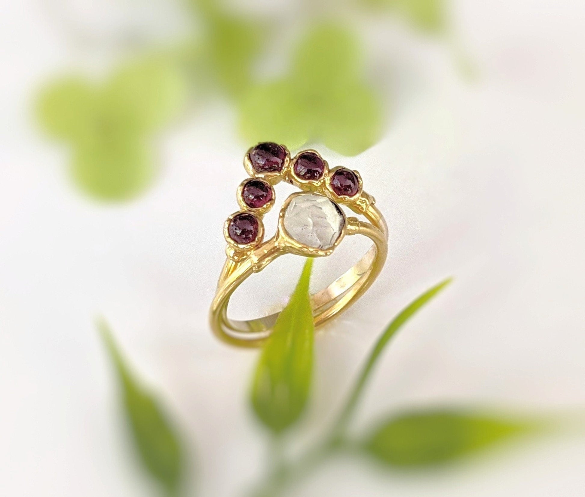 Ruby chevron ring in 18k gold with gemstones, a symbol of love and friendship, set against a soft green background.