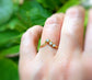 Hand wearing a raw diamond Chevron ring in 18k gold, featuring three conflict-free diamonds against a lush green background.