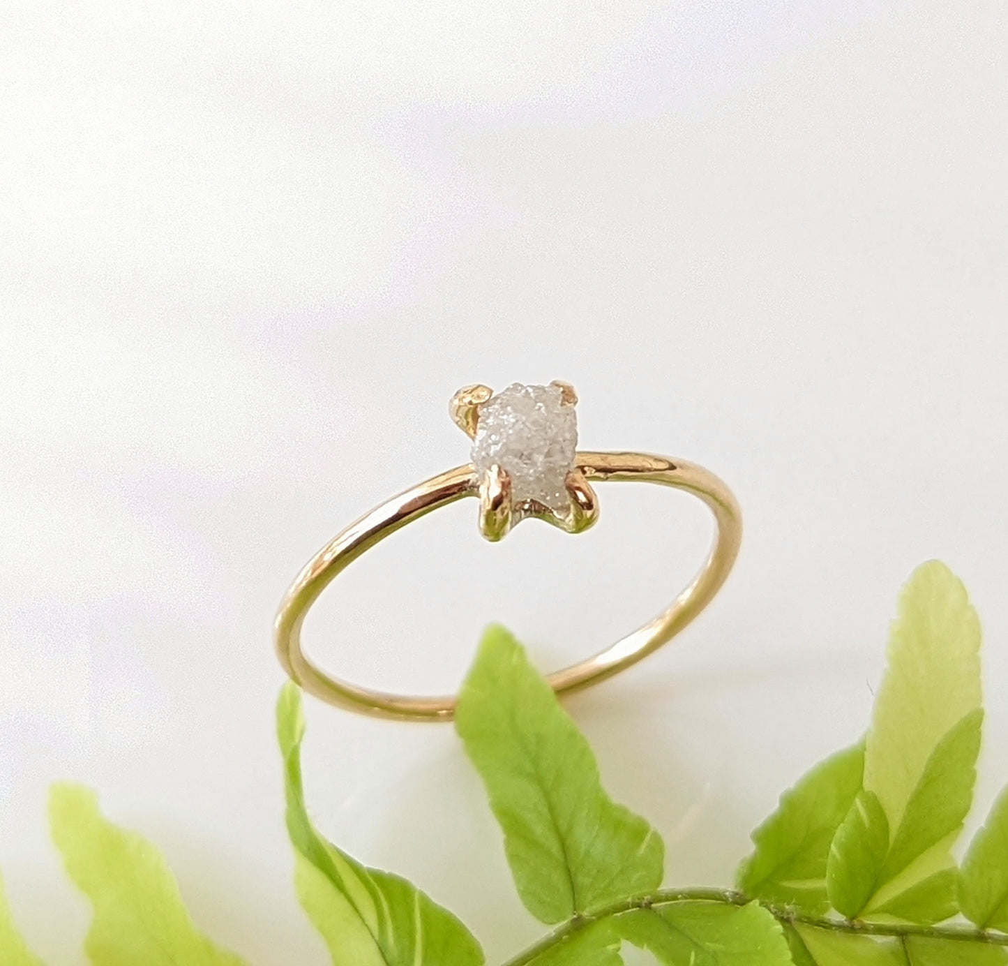Delicate raw diamond engagement ring on a gold prong band, showcasing a sparkling conflict-free diamond.