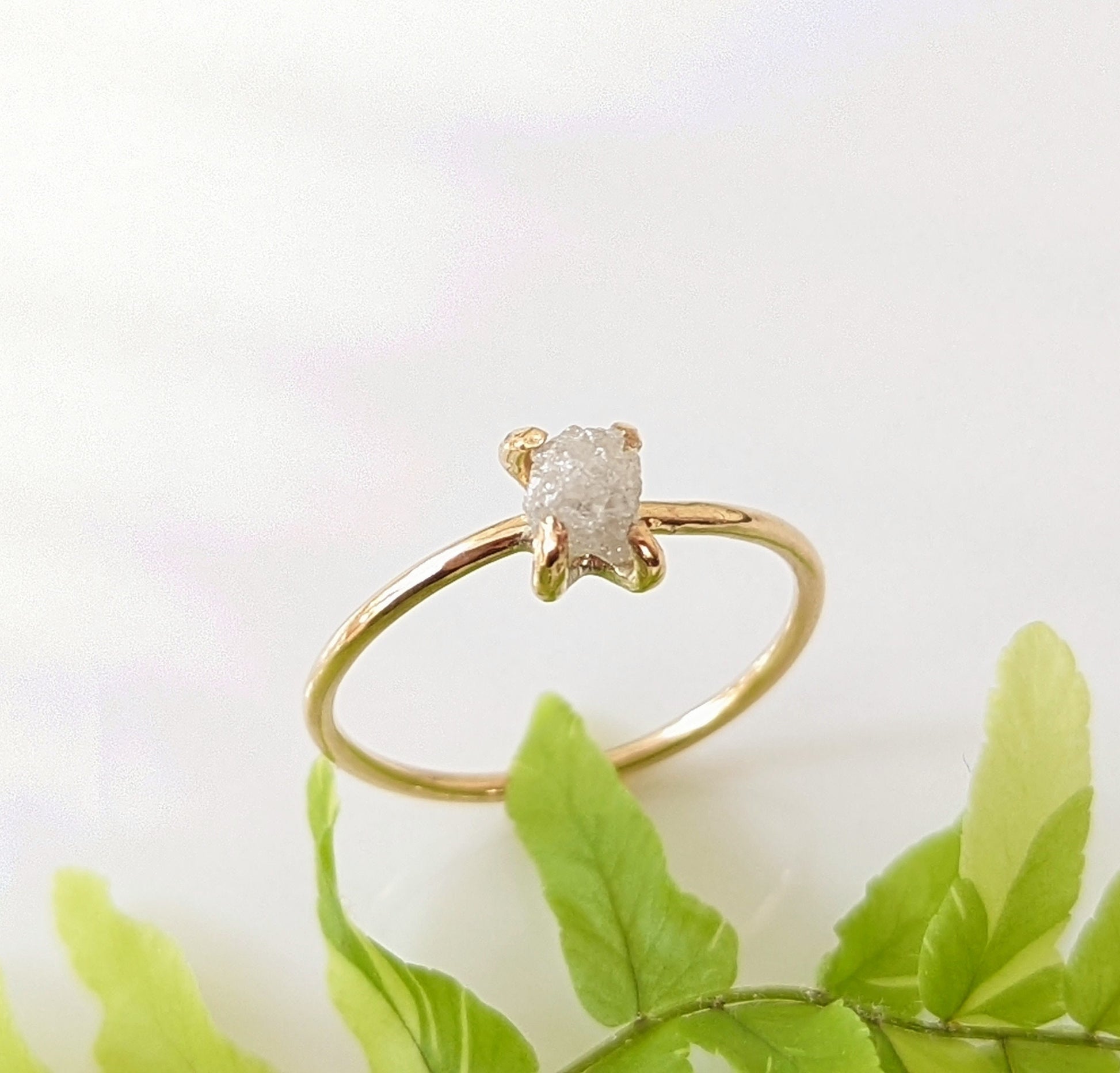 Delicate raw diamond engagement ring on a gold prong band, showcasing a sparkling conflict-free diamond.
