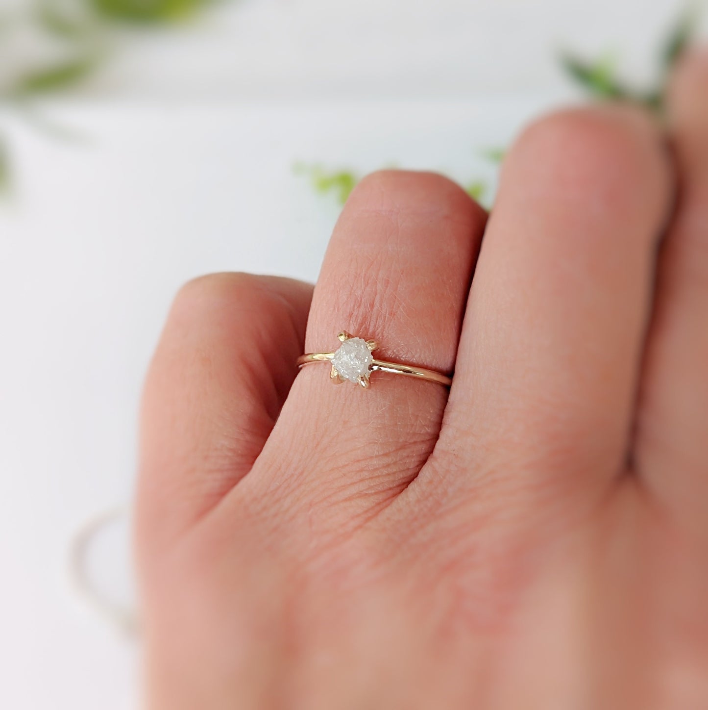 Delicate raw diamond engagement ring on a finger, featuring a 14k gold prong band and a sparkling conflict-free diamond.