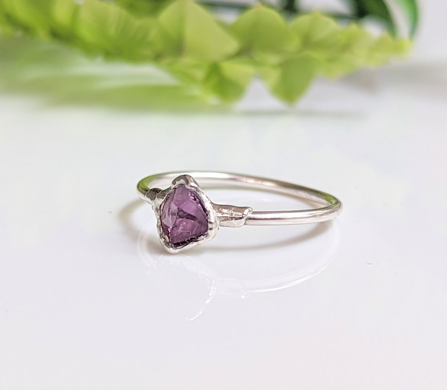 Raw Alexandrite silver ring on a reflective surface, showcasing a unique lab-grown gemstone in a sterling silver band.