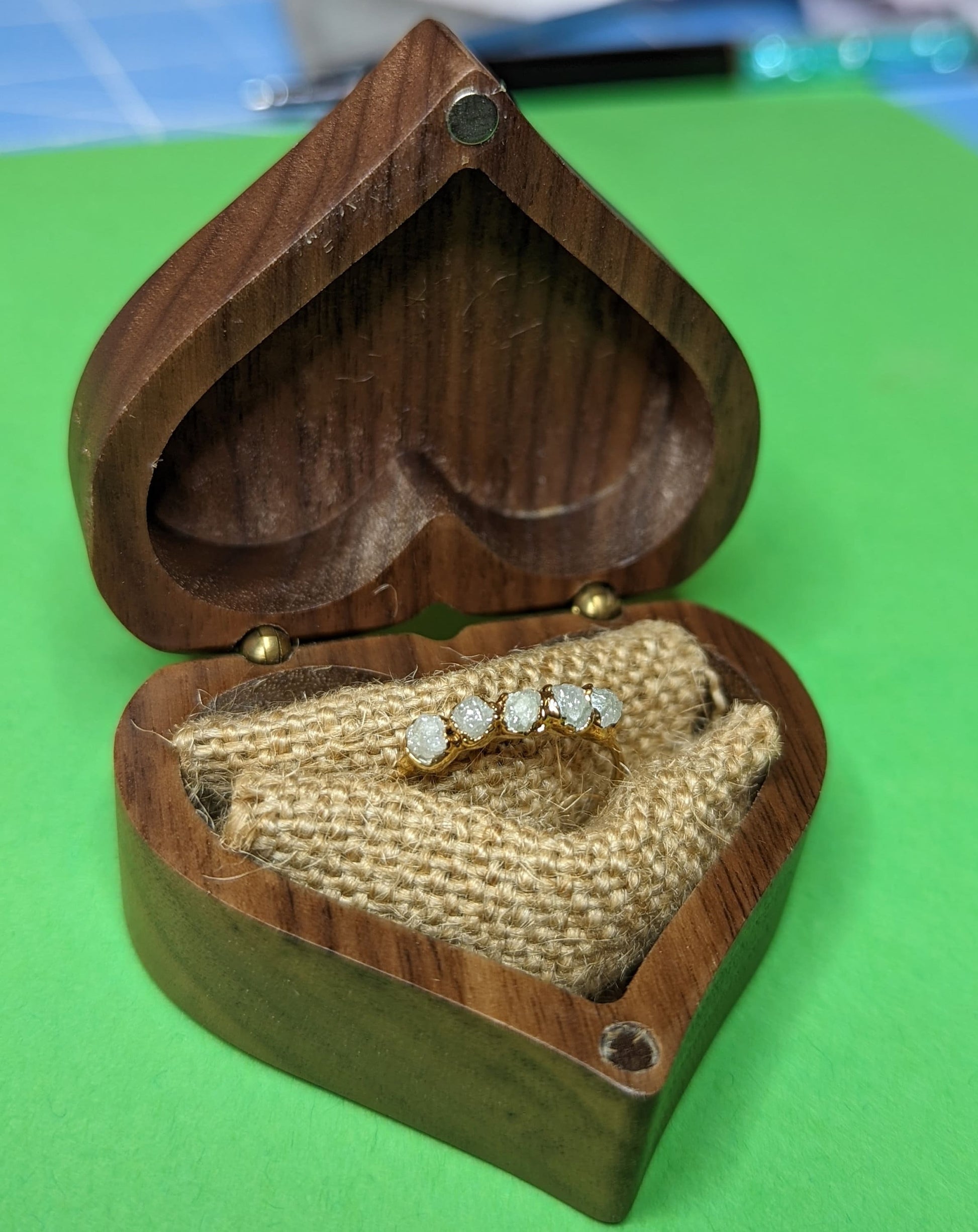 Raw diamond wedding band displayed in a heart-shaped wooden box on natural fabric.