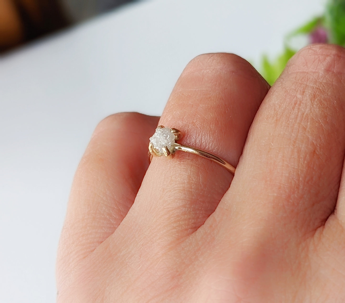 Delicate raw diamond engagement ring in 14k gold on a hand, showcasing natural beauty and timeless elegance.